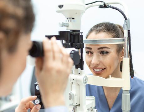 Eye doctor examining a smiling patient with a slit lamp in a clinic