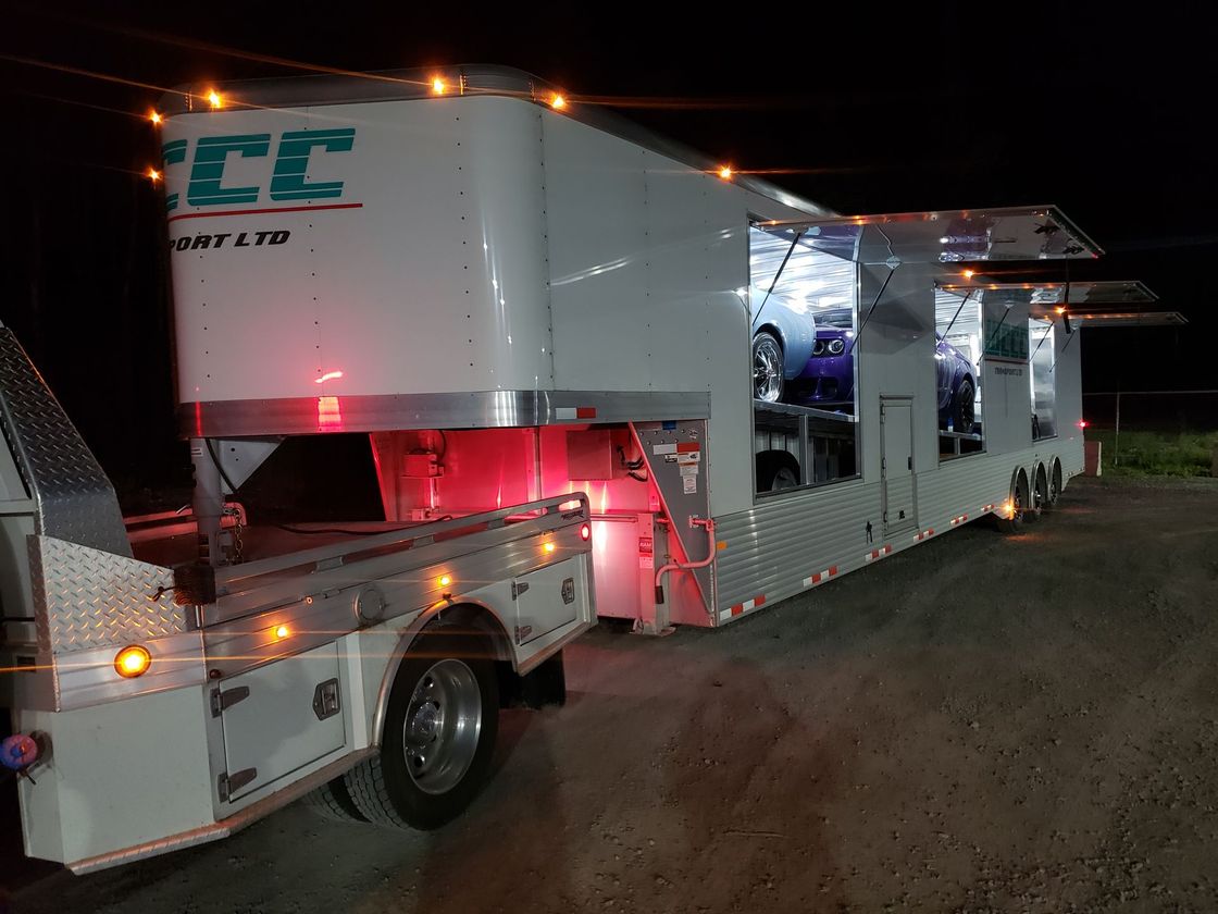 A trailer with cars on it is parked in a parking lot at night.