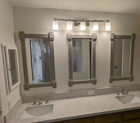 Bathroom with three framed mirrors above a countertop with sinks and a light fixture.