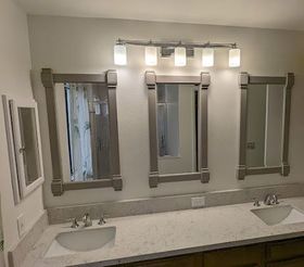Bathroom with three framed mirrors above a countertop with sinks and a light fixture.