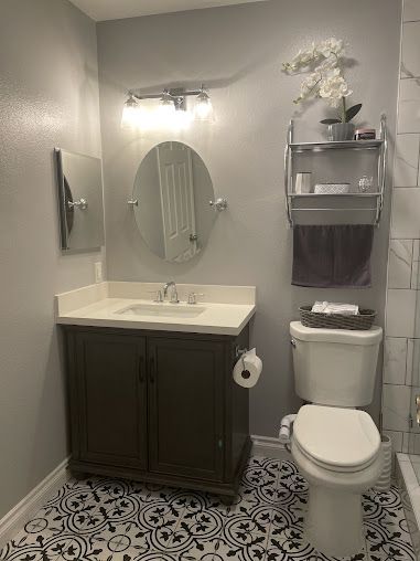 Bathroom with vanity, toilet, and patterned floor. Silver fixtures, gray walls, and white countertop.