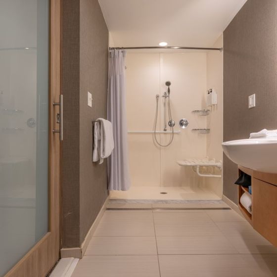 Accessible bathroom with marble tile shower, grab bars, and raised toilet. Gray hexagon tile floor.