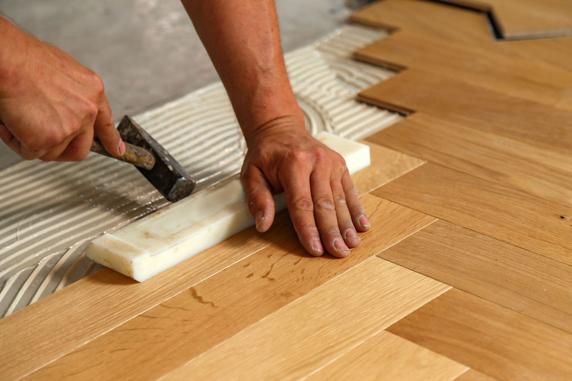 Hands installing a wooden floor with adhesive trowel and parquet planks
