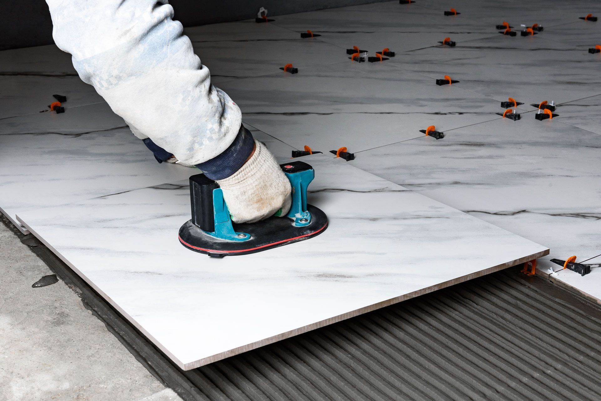 Worker using a power sander on a large white floor tile during installation
