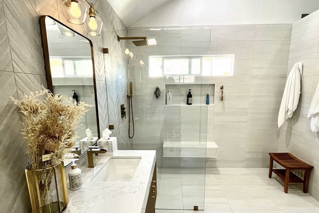 Modern bathroom with herringbone tile, glass shower, marble vanity, and gold fixtures.