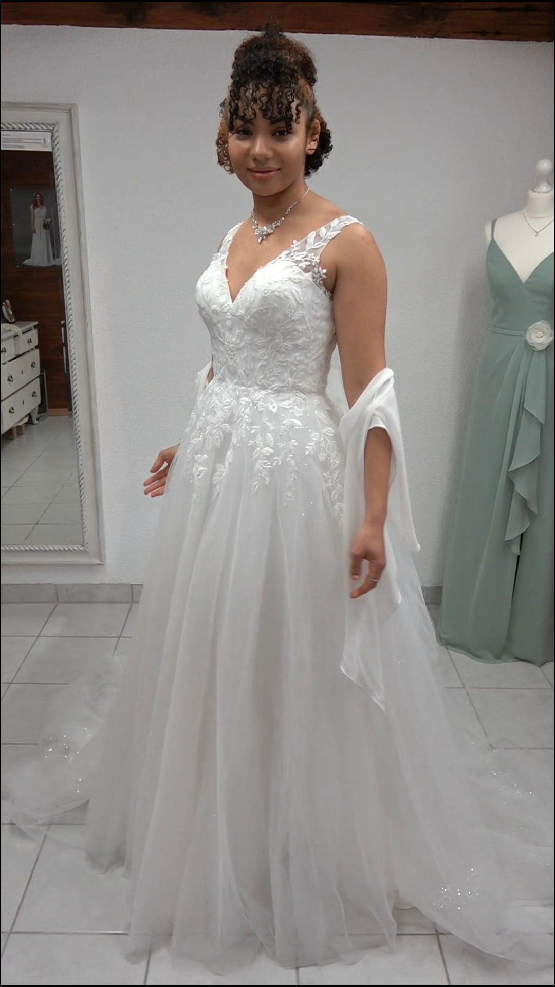 Frau in einem weißen, perlenbesetzten Brautkleid steht in einem Brautmodengeschäft