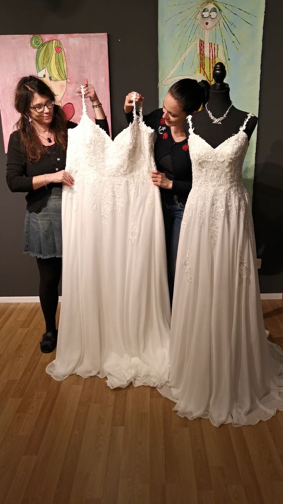 Eine Frau steht neben zwei weißen Brautkleidern auf Schaufensterpuppen in einem Boutique-Showroom.