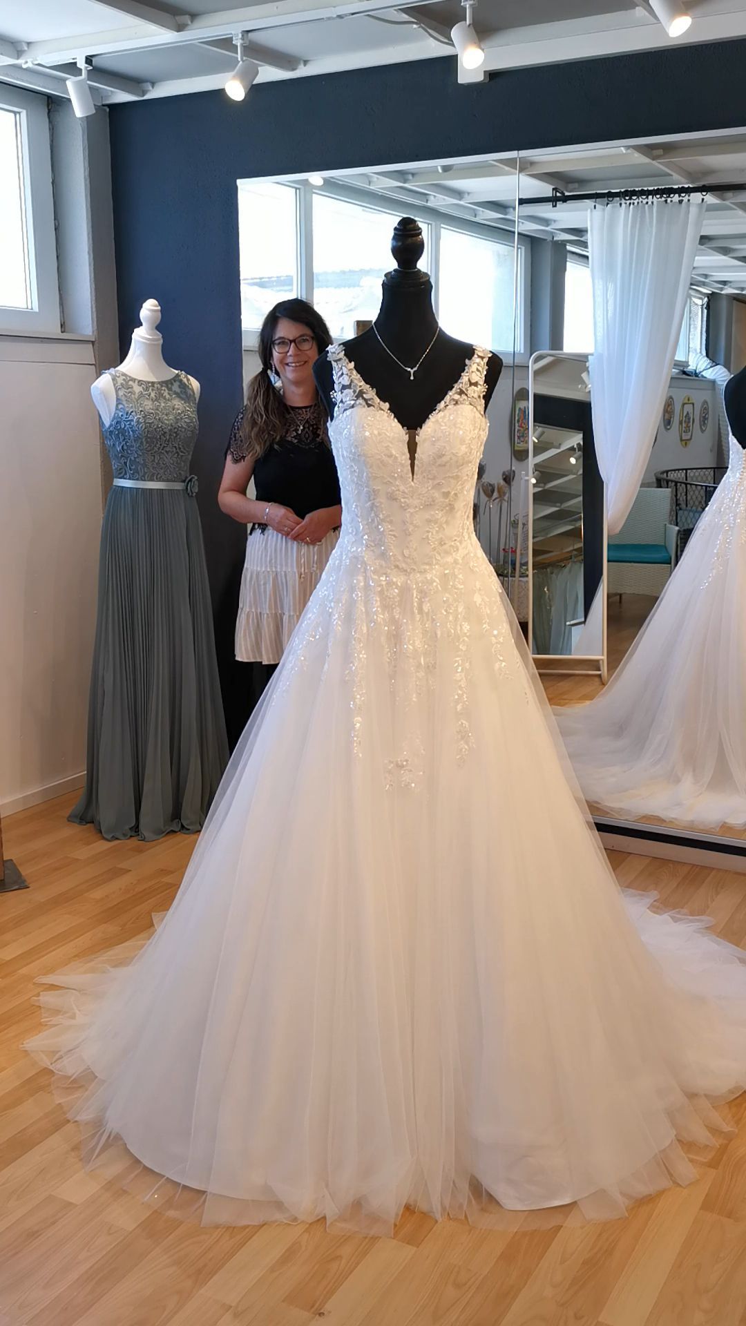 Brautmodengeschäft mit einem weißen Brautkleid an einer Schaufensterpuppe und einer daneben stehenden Frau