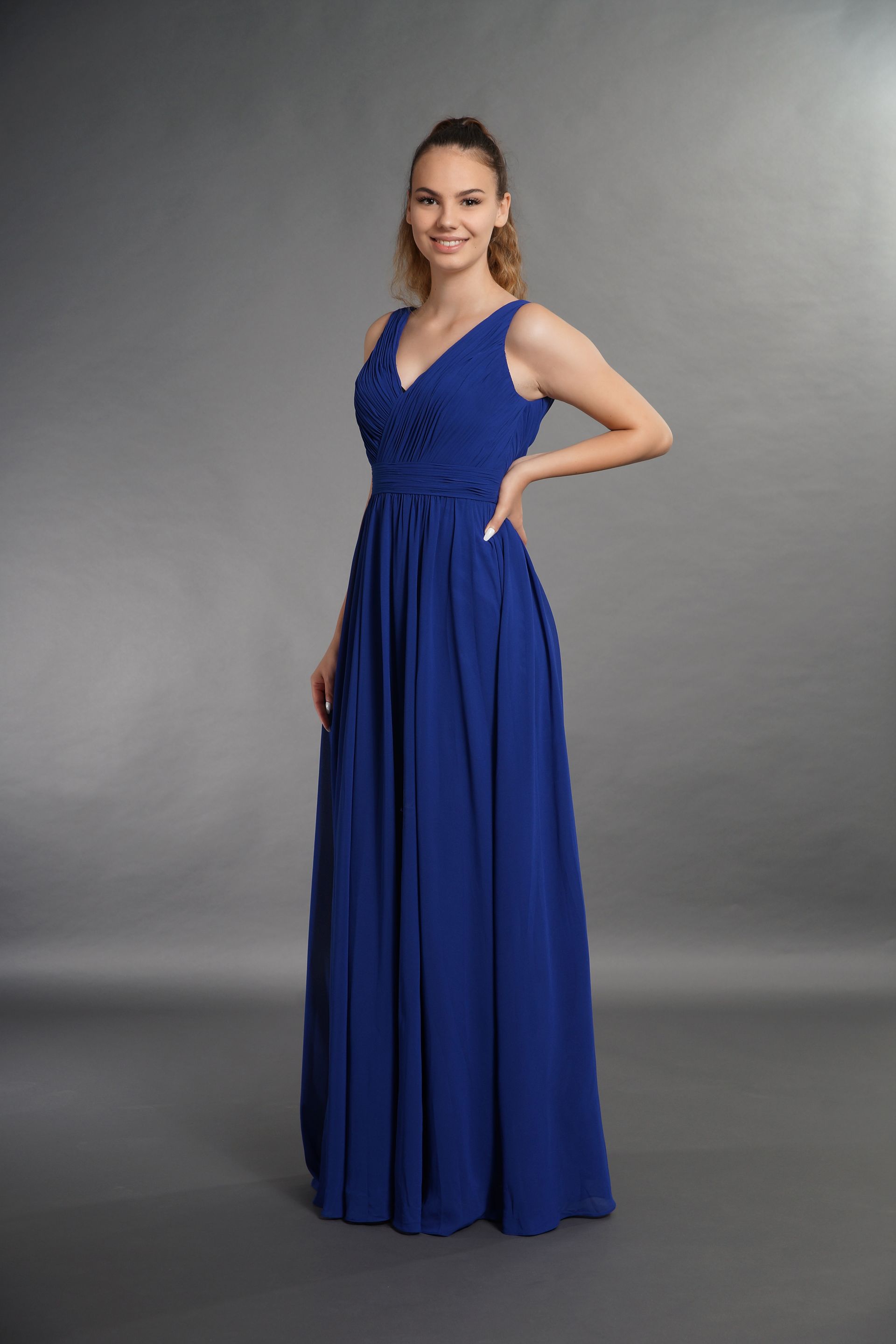 Frau in einem langen blauen Kleid vor grauem Studiohintergrund.