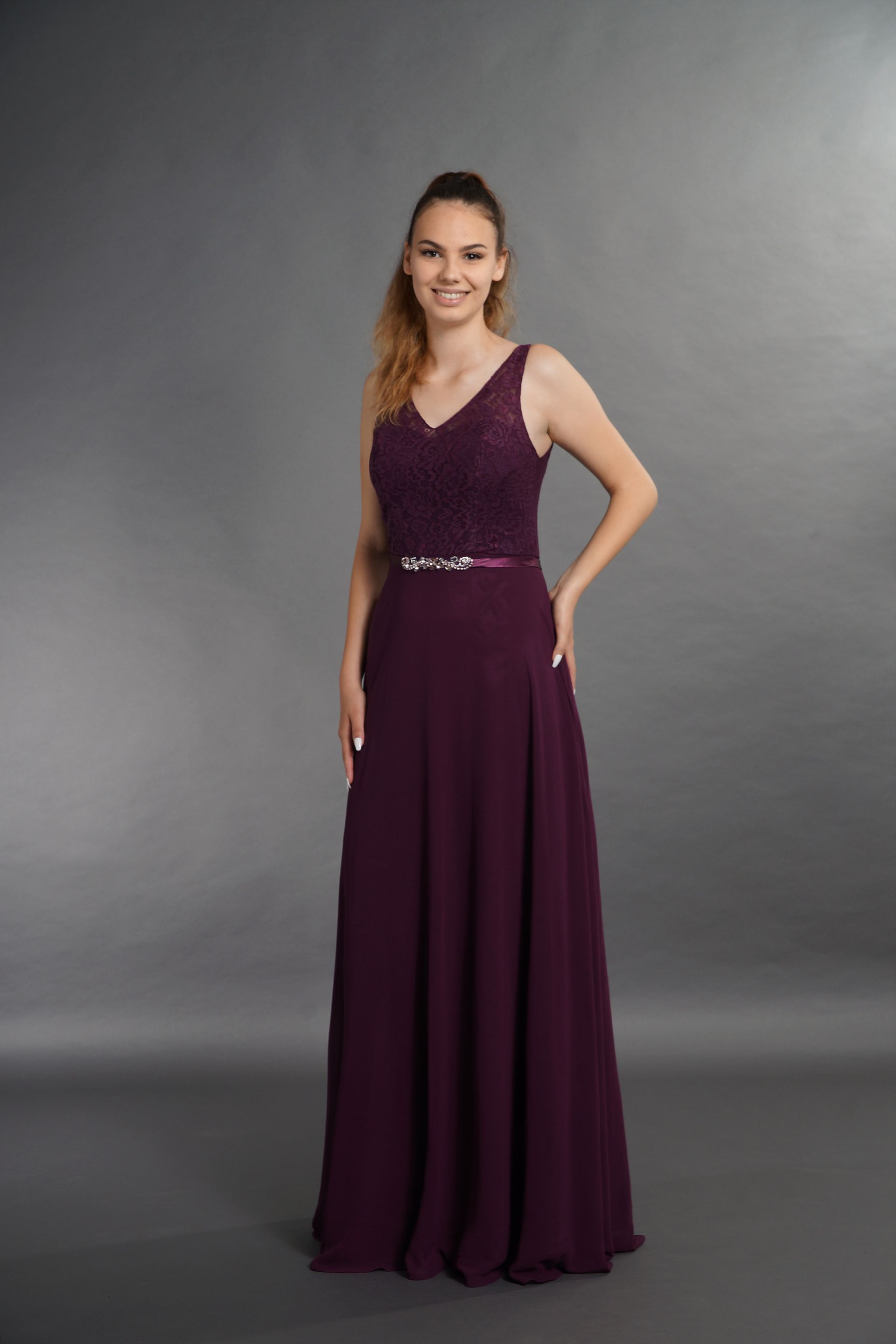 Frau in einem ärmellosen, violetten Abendkleid vor grauem Studiohintergrund.