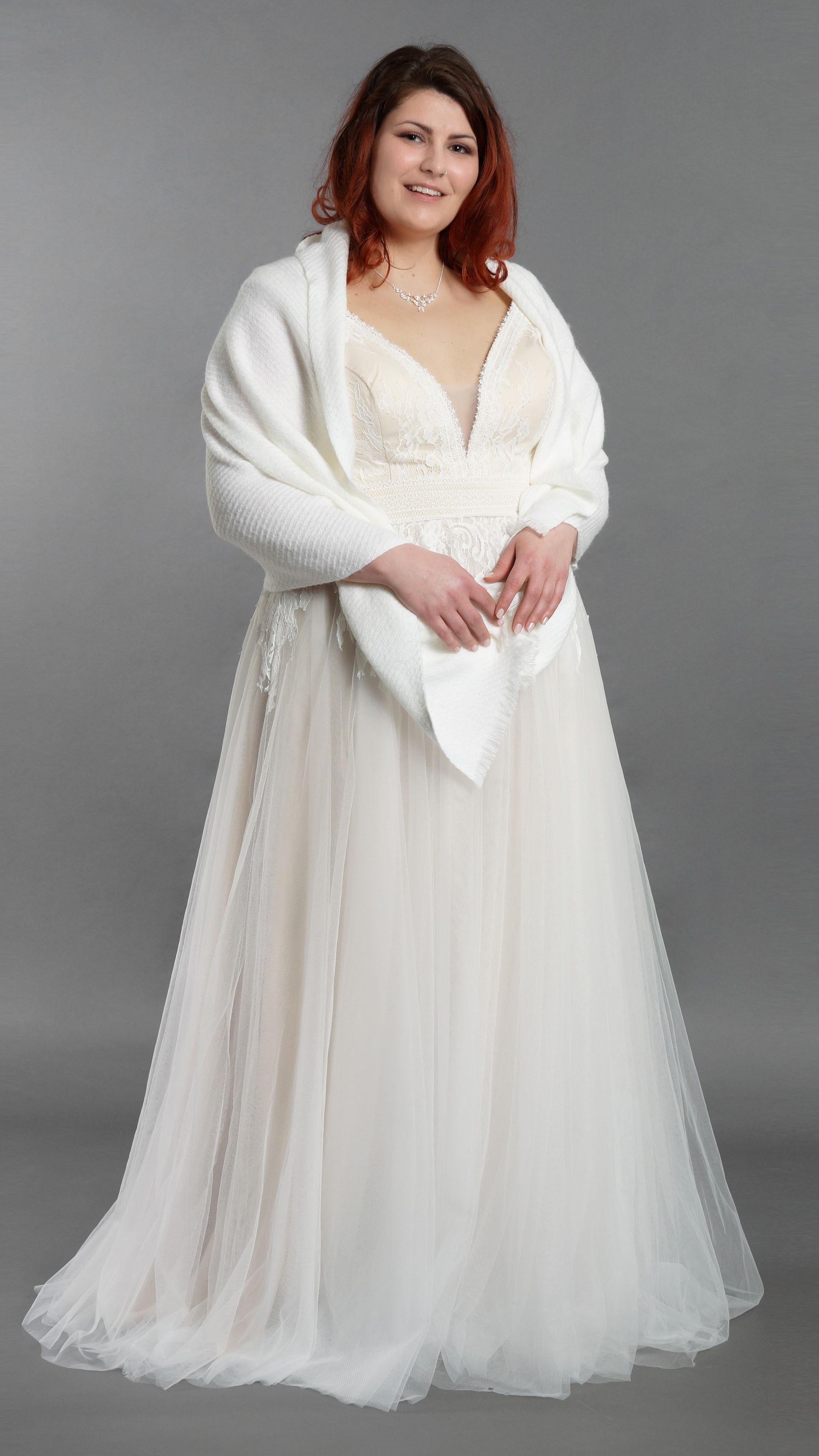 Frau in weißem Brautkleid und Schal vor grauem Studiohintergrund