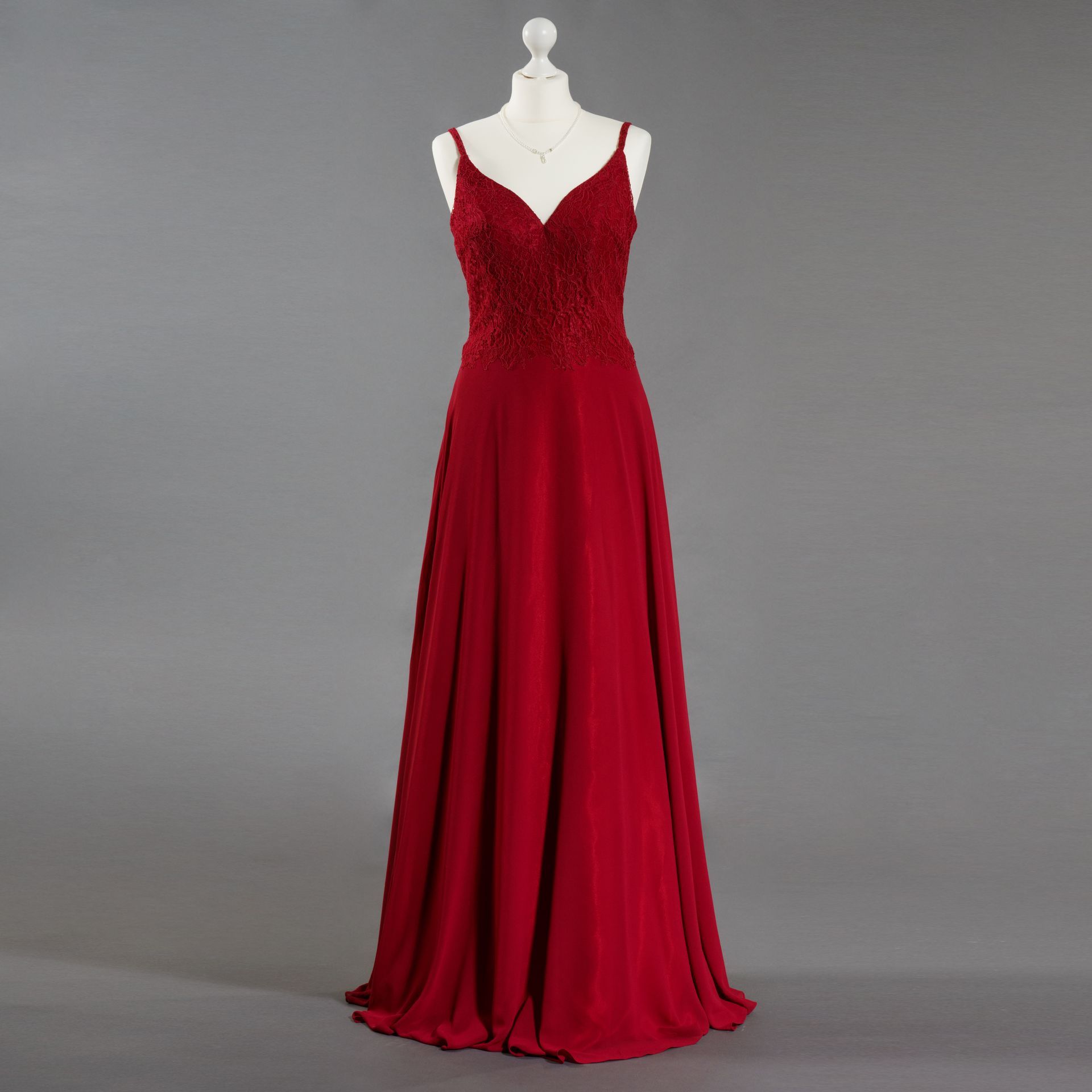 Rotes, bodenlanges Abendkleid mit Spaghettiträgern an einer Schaufensterpuppe vor grauem Hintergrund