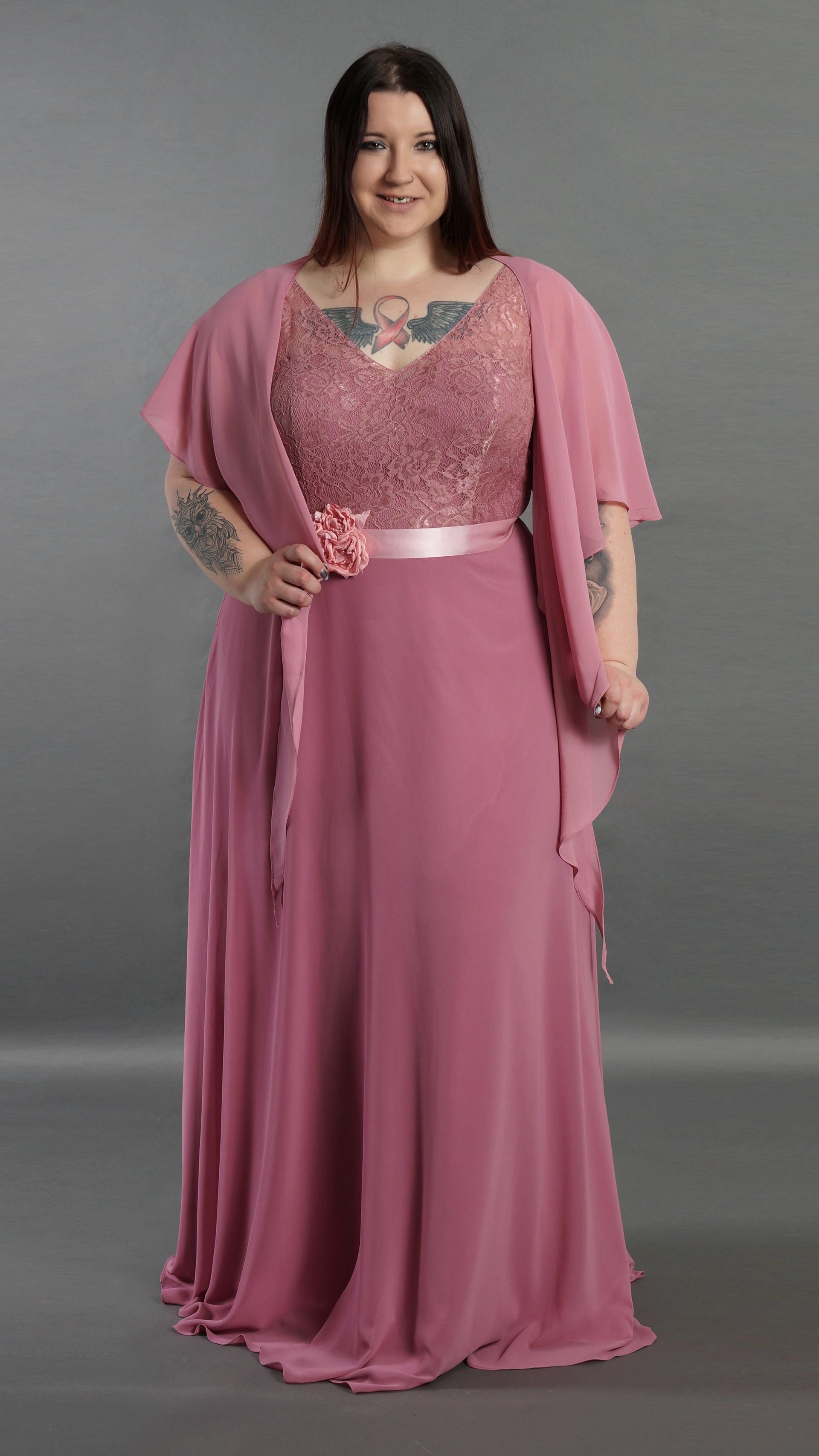 Frau in einem pinkfarbenen, verzierten Kleid vor grauem Studiohintergrund
