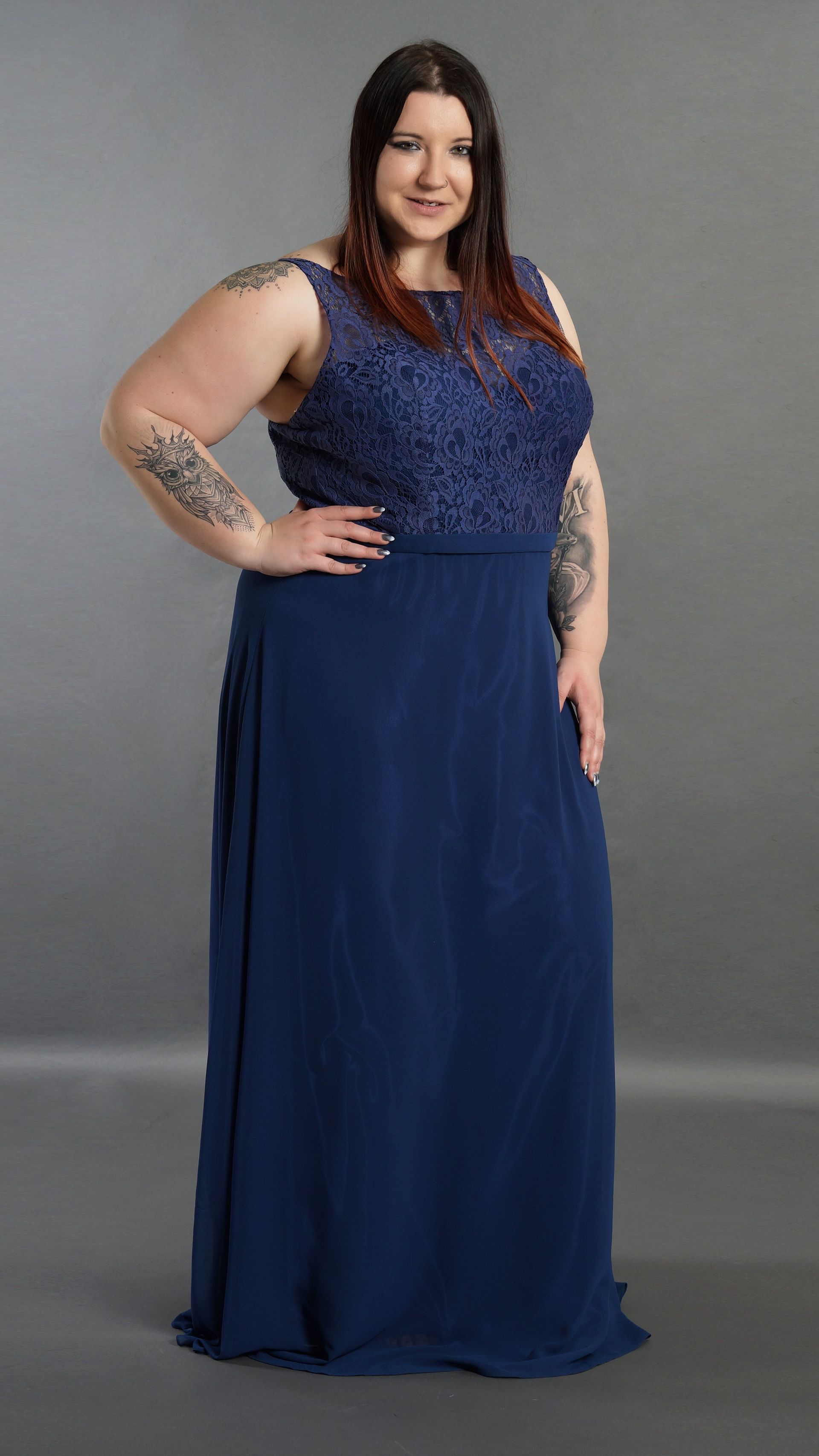 Frau in einem marineblauen Kleid posiert vor einem grauen Hintergrund.