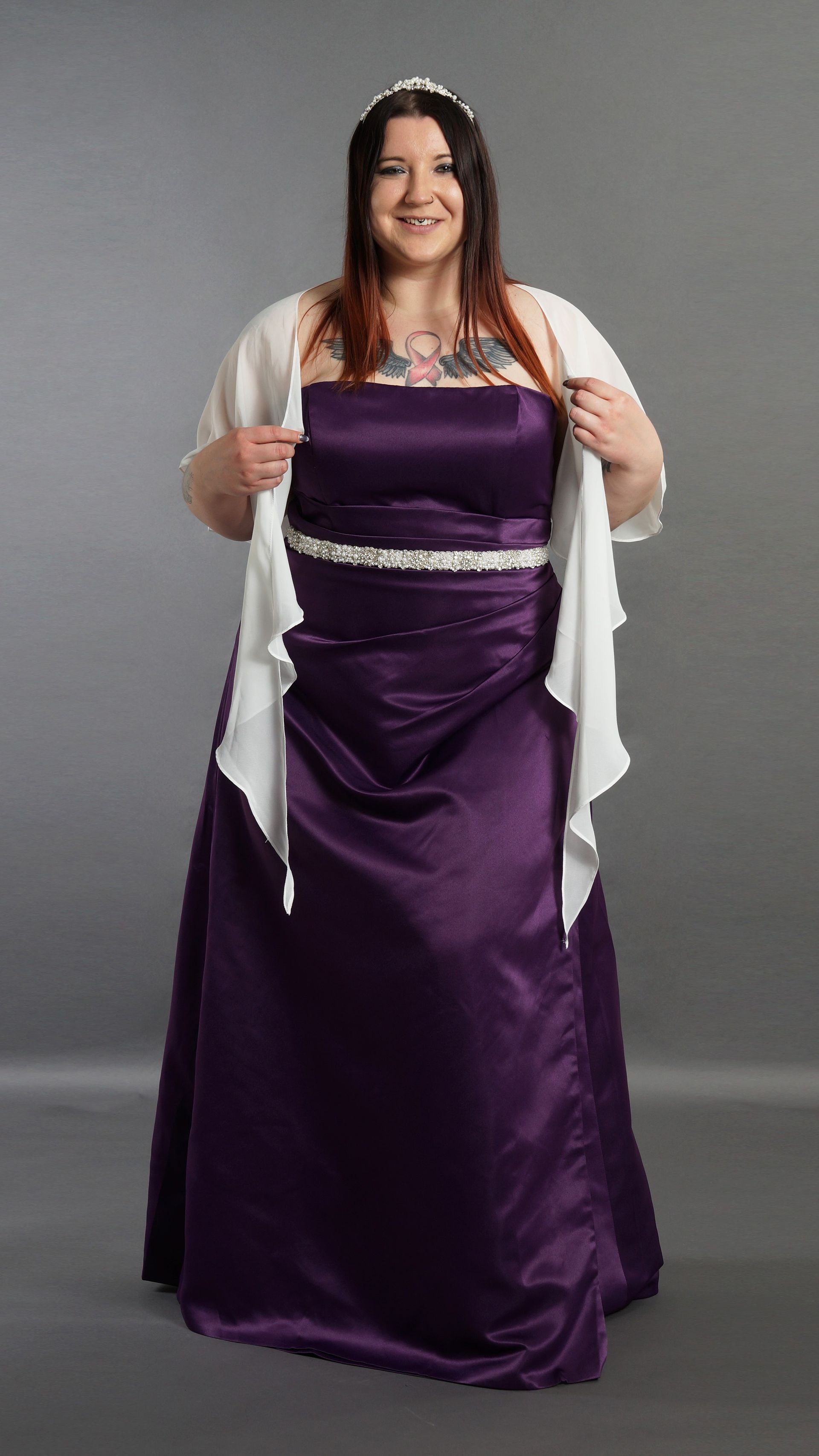 Frau in einem lila trägerlosen Kleid hält einen weißen Schal vor grauem Hintergrund.