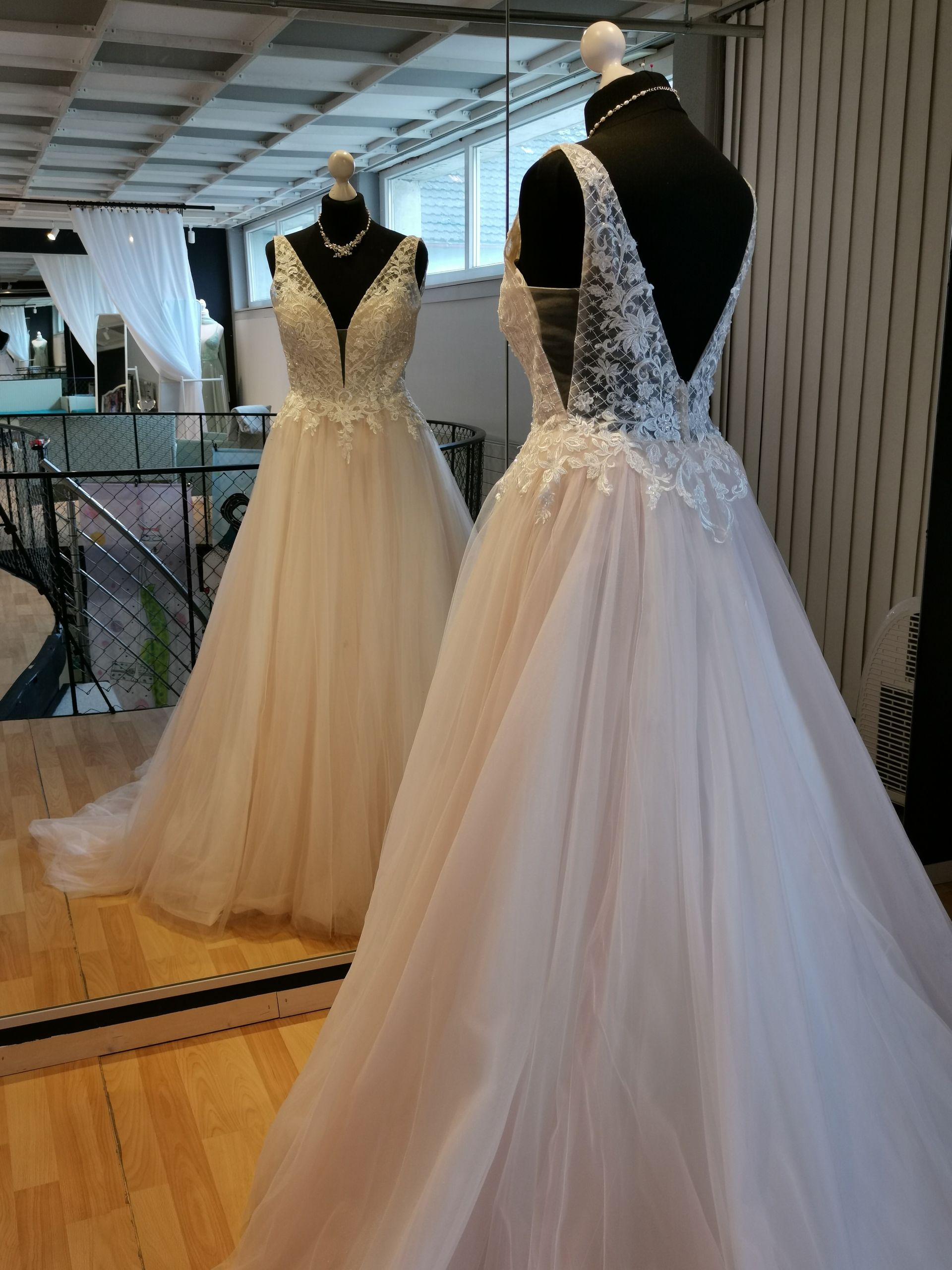 Weißes Brautkleid mit Spitzenoberteil und Tüllrock, ausgestellt an einer Schaufensterpuppe vor einem Spiegel im Ausstellungsraum.