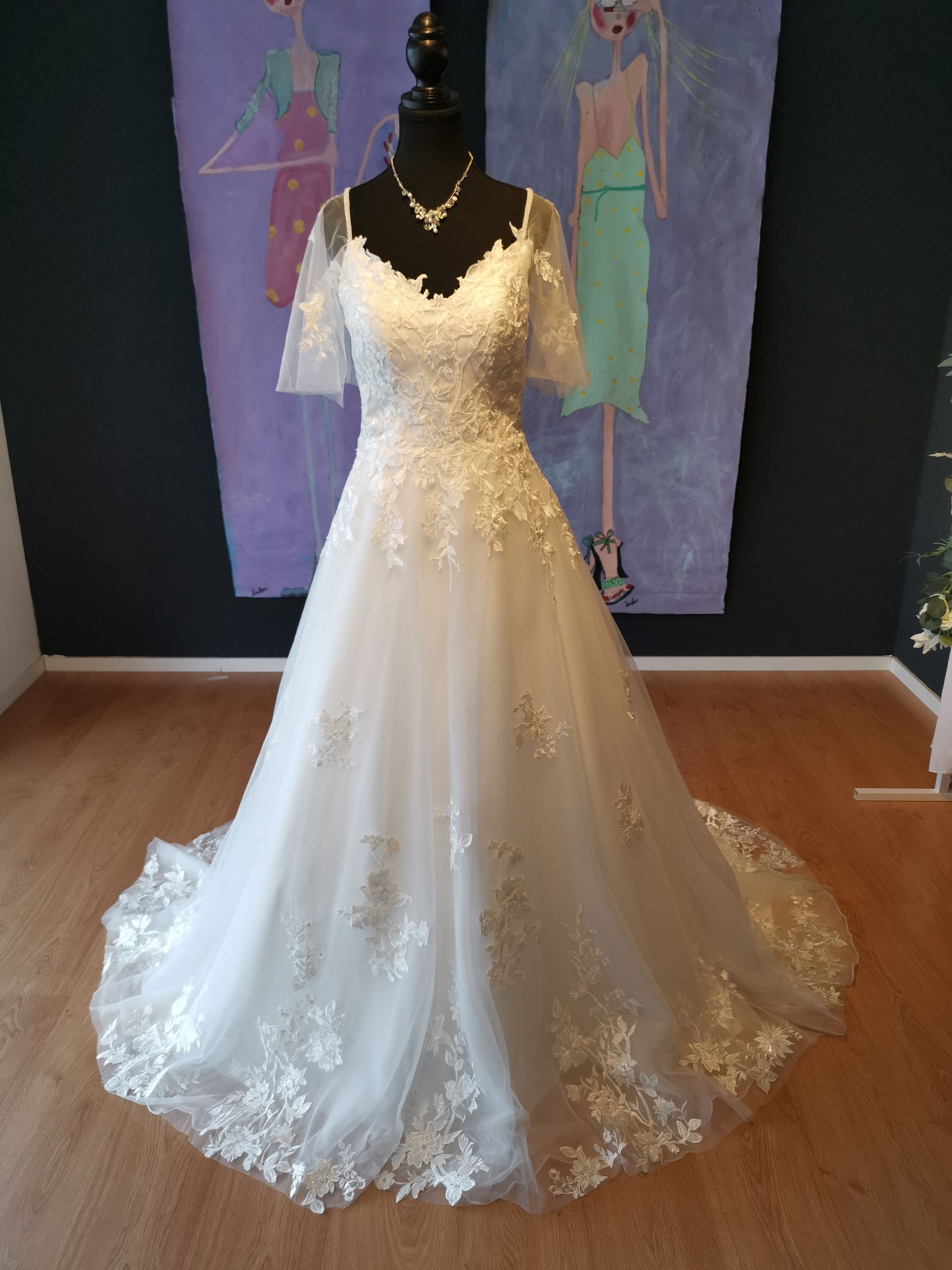Weißes Brautkleid aus Spitze an einer Schaufensterpuppe in einem Ausstellungsraum, mit voluminösem Rock und Schleppe.