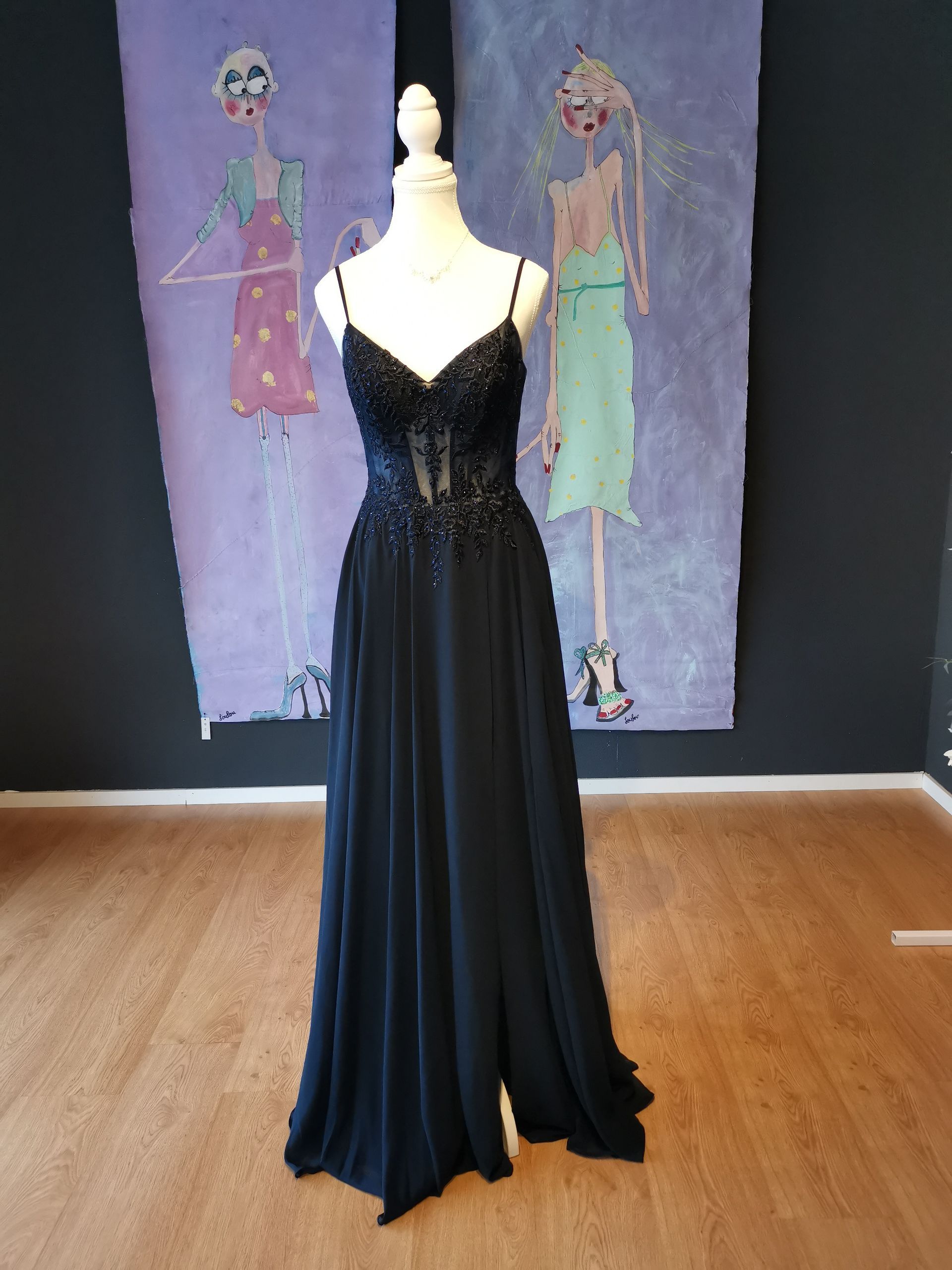 Schwarzes, ärmelloses Abendkleid auf einer Schaufensterpuppe vor einem Wandgemälde mit zwei Figuren