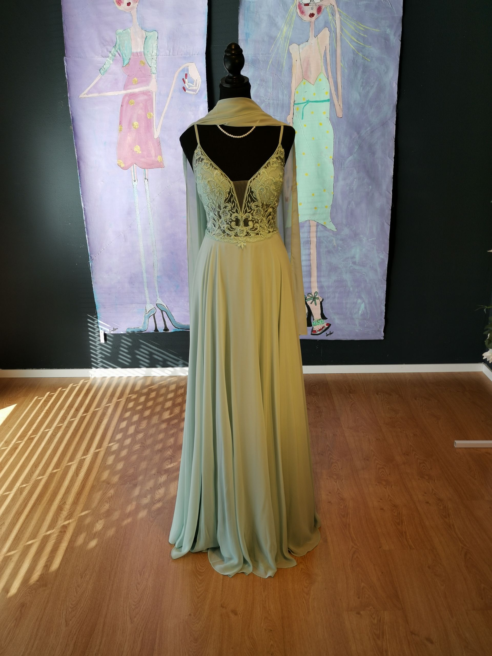 Schaufensterpuppe in einem schwarz-goldenen Abendkleid in einer Galerie, im Hintergrund farbenfrohe Textilkunst