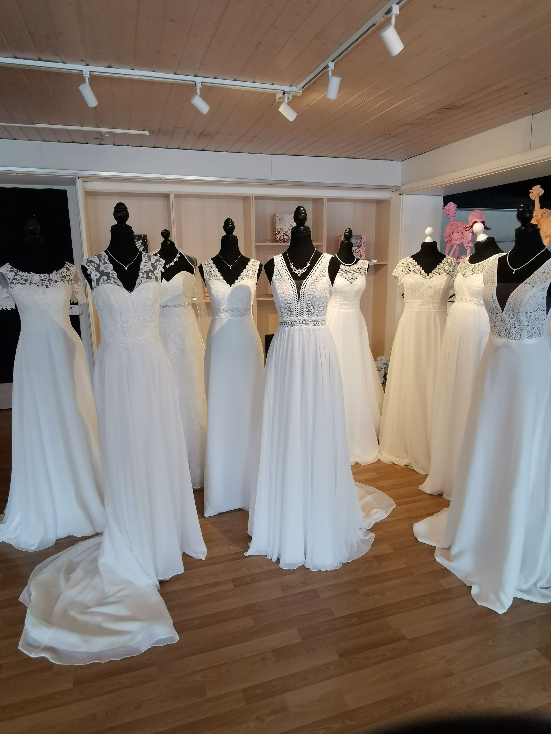 Weiße Brautkleider werden auf Schaufensterpuppen in einer hellen Boutique mit Holzboden und Schienenbeleuchtung präsentiert.