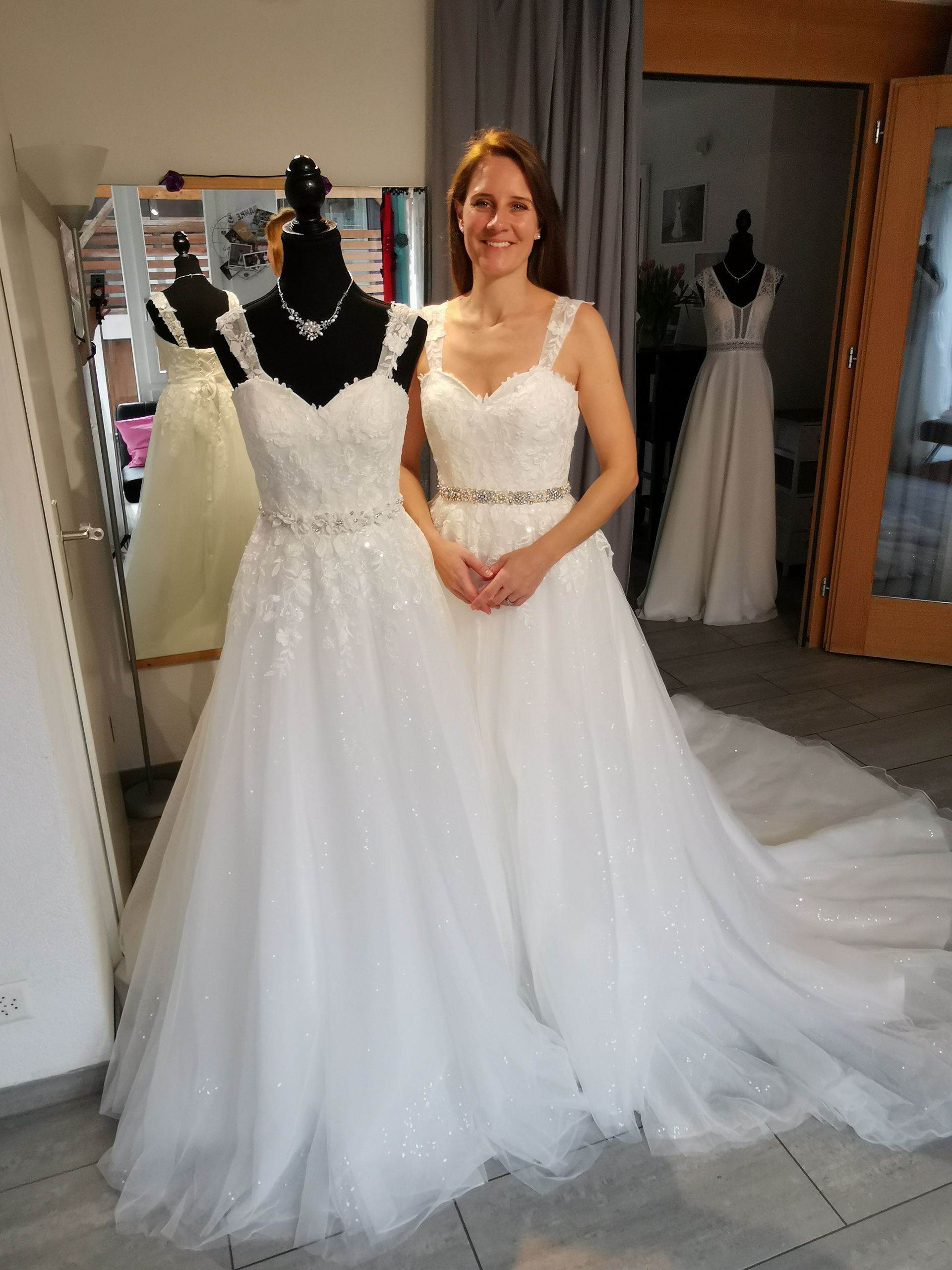 Frau in einem weißen Brautkleid steht neben einer Schaufensterpuppe, die ein Brautkleid in einem Brautmodengeschäft präsentiert.