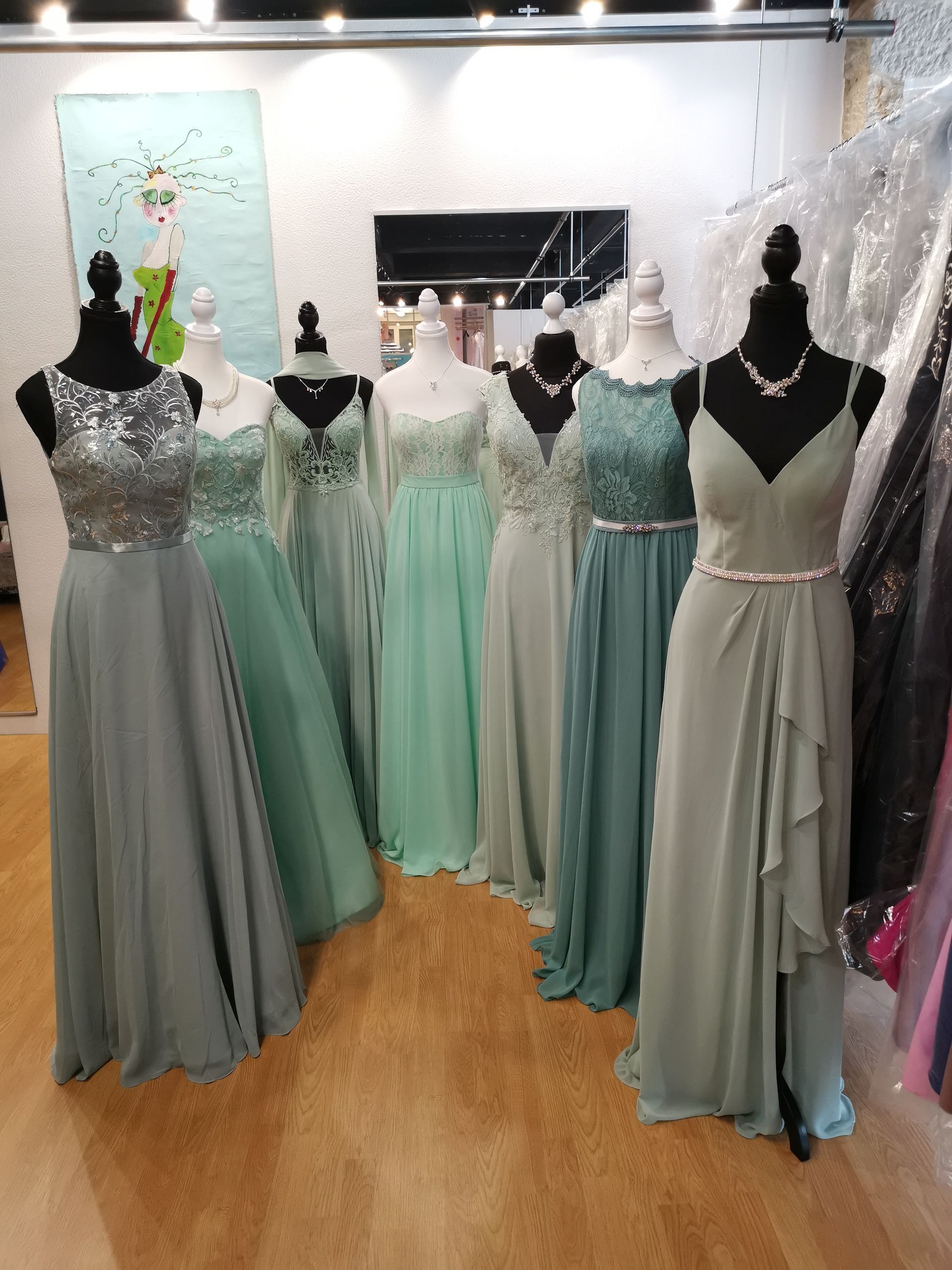 Schaufensterpuppen präsentieren pastellgrüne und graue Abendkleider in einem Boutique-Showroom