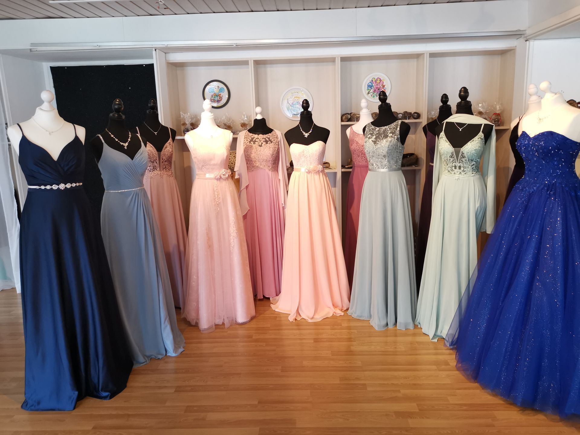 Eine Reihe von pastellfarbenen und marineblauen Abendkleidern, ausgestellt an Schaufensterpuppen in einer Boutique