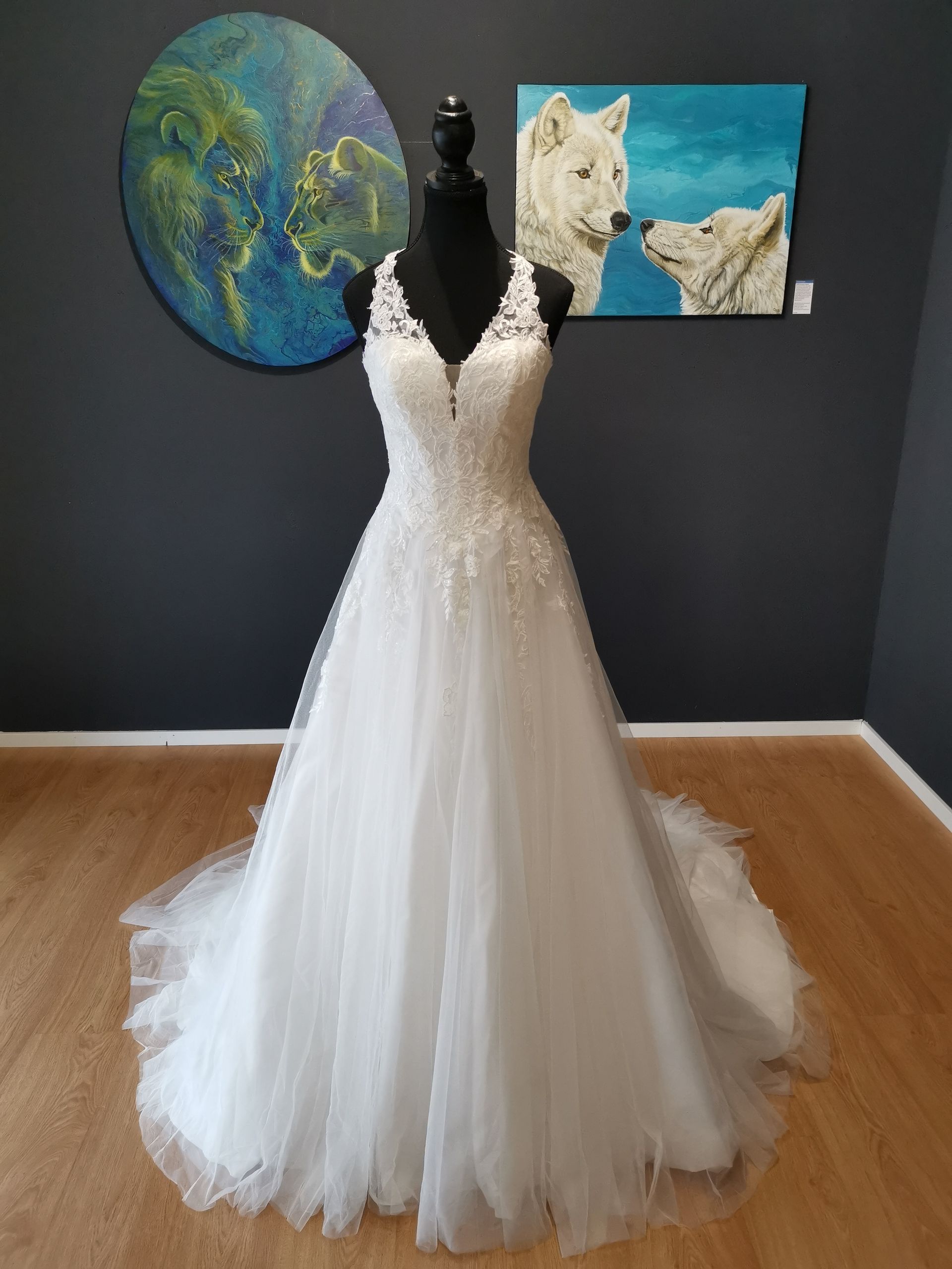 Weißes Brautkleid auf einer Schaufensterpuppe in einer Galerie, dahinter zwei Gemälde an einer dunklen Wand
