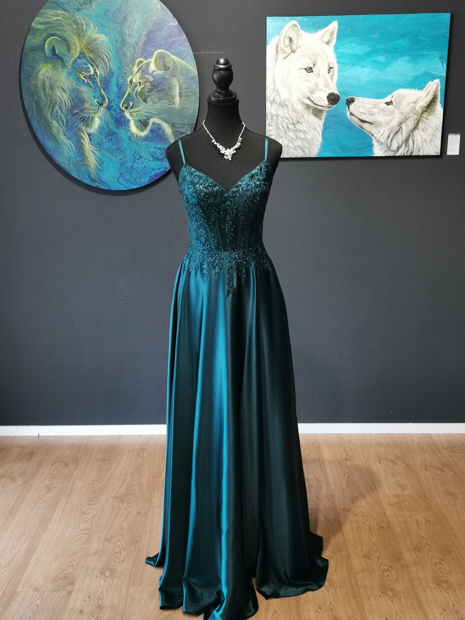 Türkisfarbenes Satin-Abendkleid an einer Schaufensterpuppe in einer Galerie mit abstrakten Gemälden und Wolfsmotiven an einer dunklen Wand