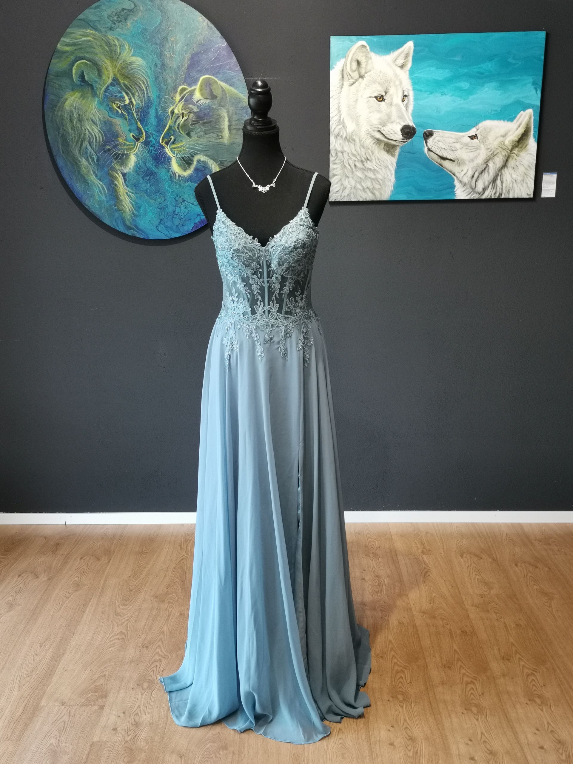 Hellblaues Abendkleid auf einer Schaufensterpuppe in einer Galerie mit zwei Gemälden an einer dunklen Wand.