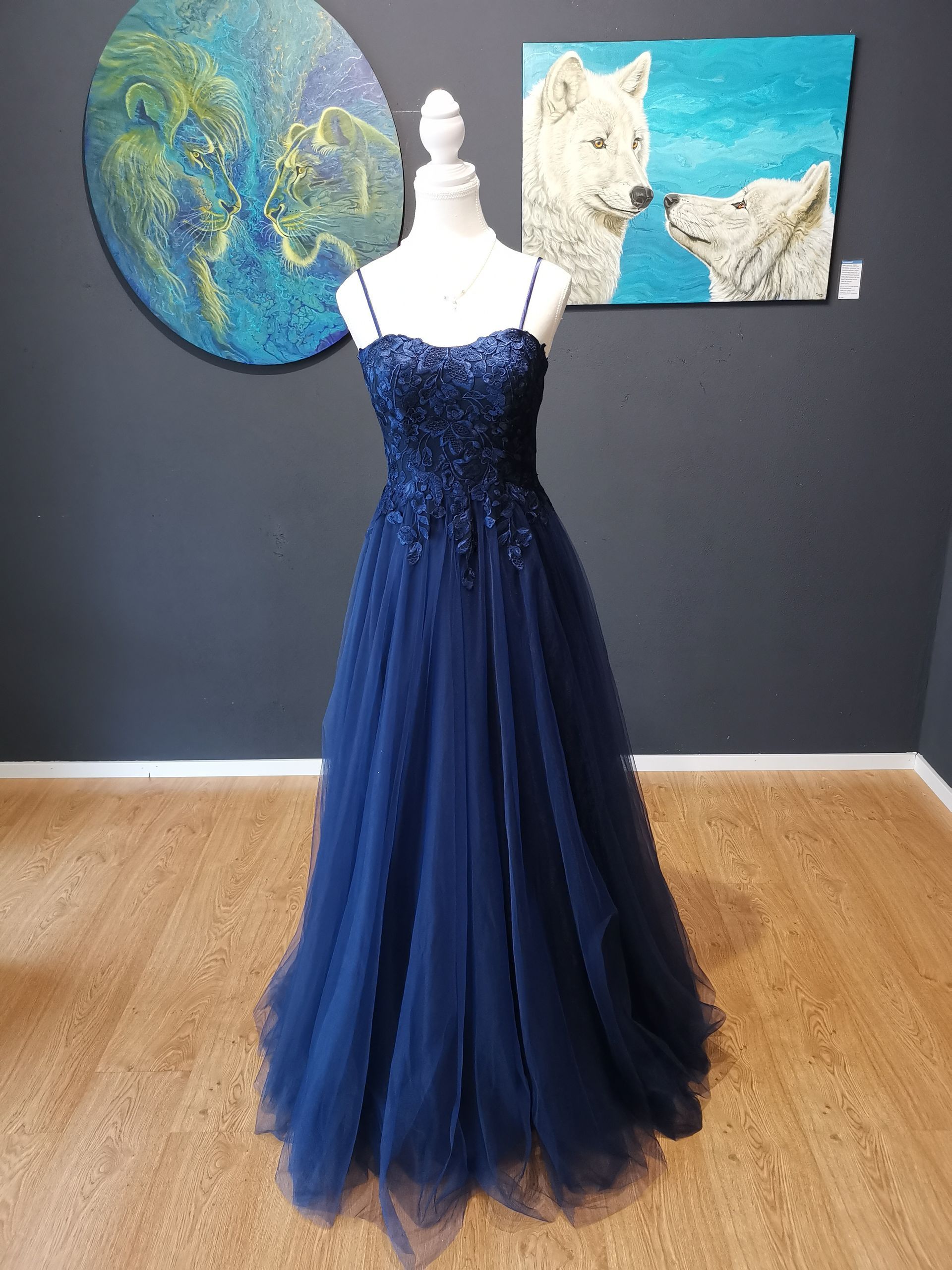 Marineblaues Abendkleid auf einer Schaufensterpuppe vor einer Wand mit Kunstwerken.