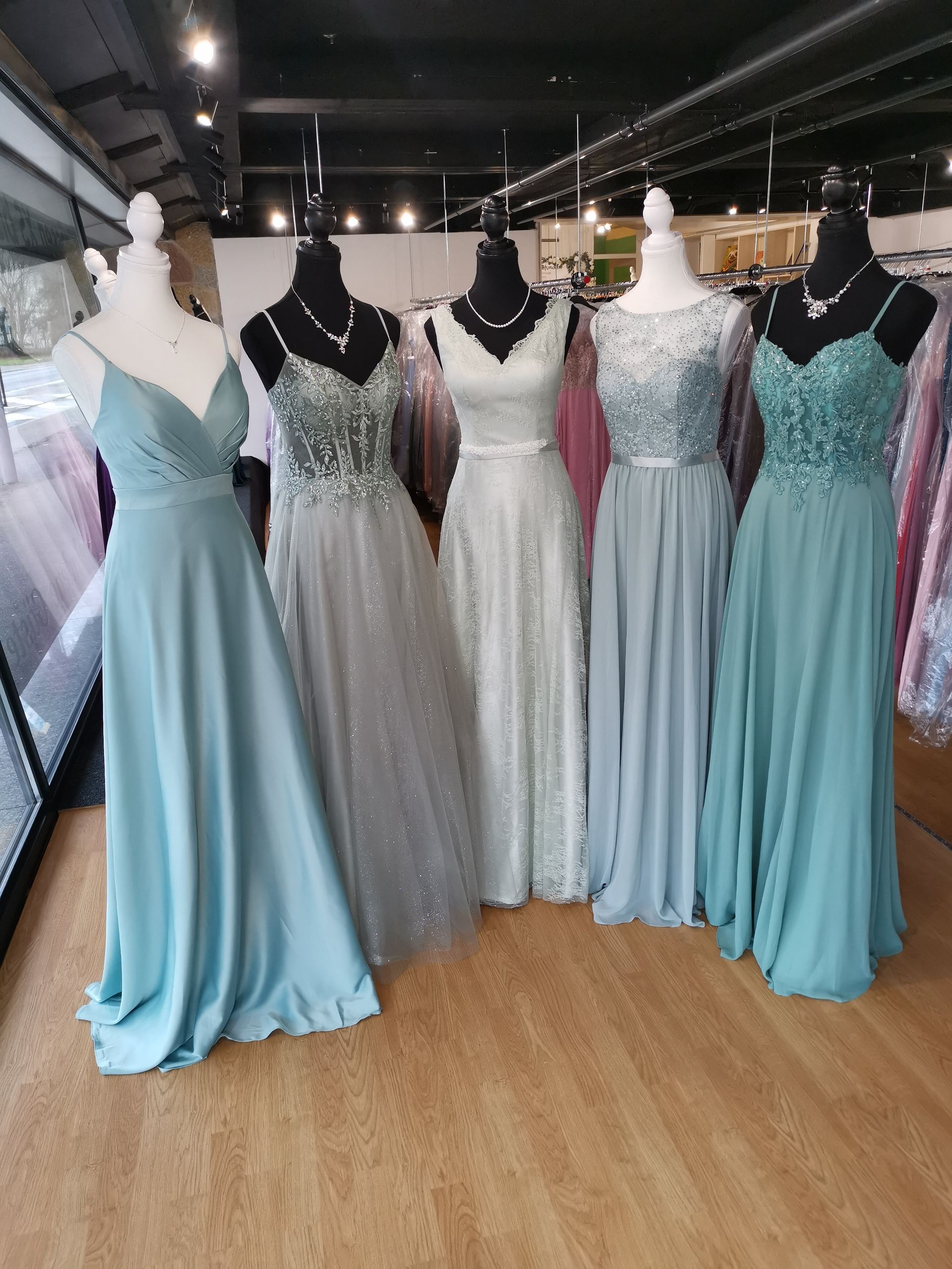 Schaufensterpuppen in einem Brautmodengeschäft, die pastellblaue und silberne Abendkleider tragen.
