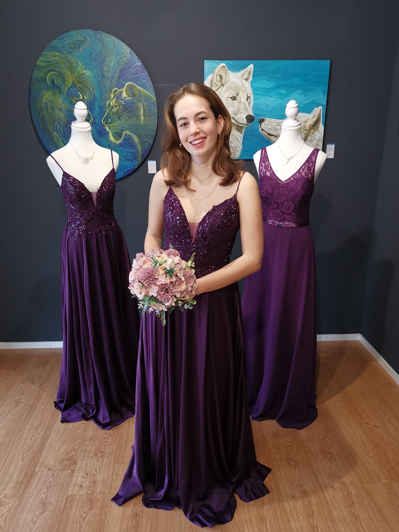 Frau in lila Kleid hält Blumenstrauß zwischen zwei lila Kleidern auf Schaufensterpuppen in einem Studio