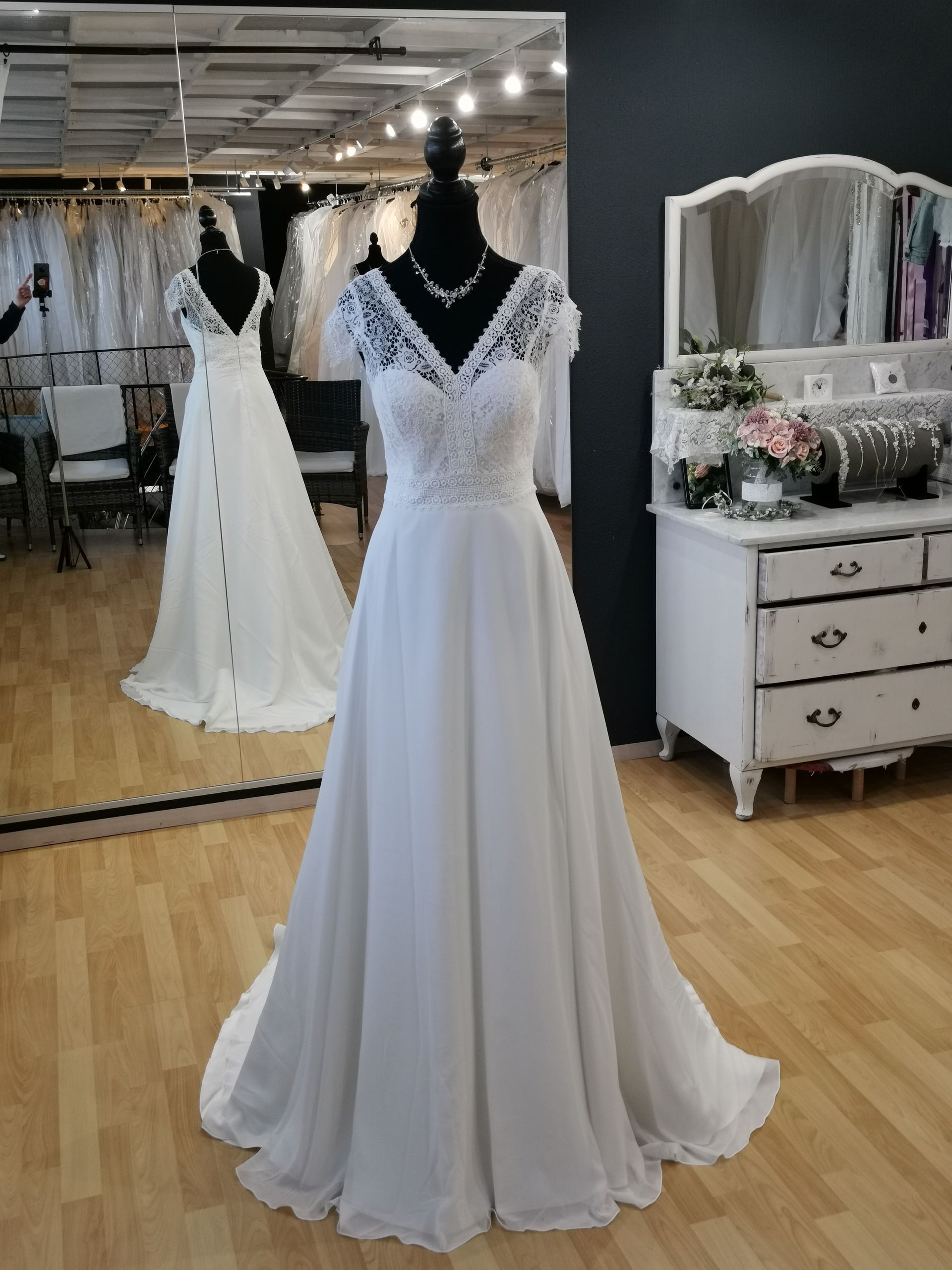 Weißes Spitzenhochzeitskleid an einer Schaufensterpuppe in einer Brautboutique, mit Spiegelreflexion und Kleiderpräsentation.