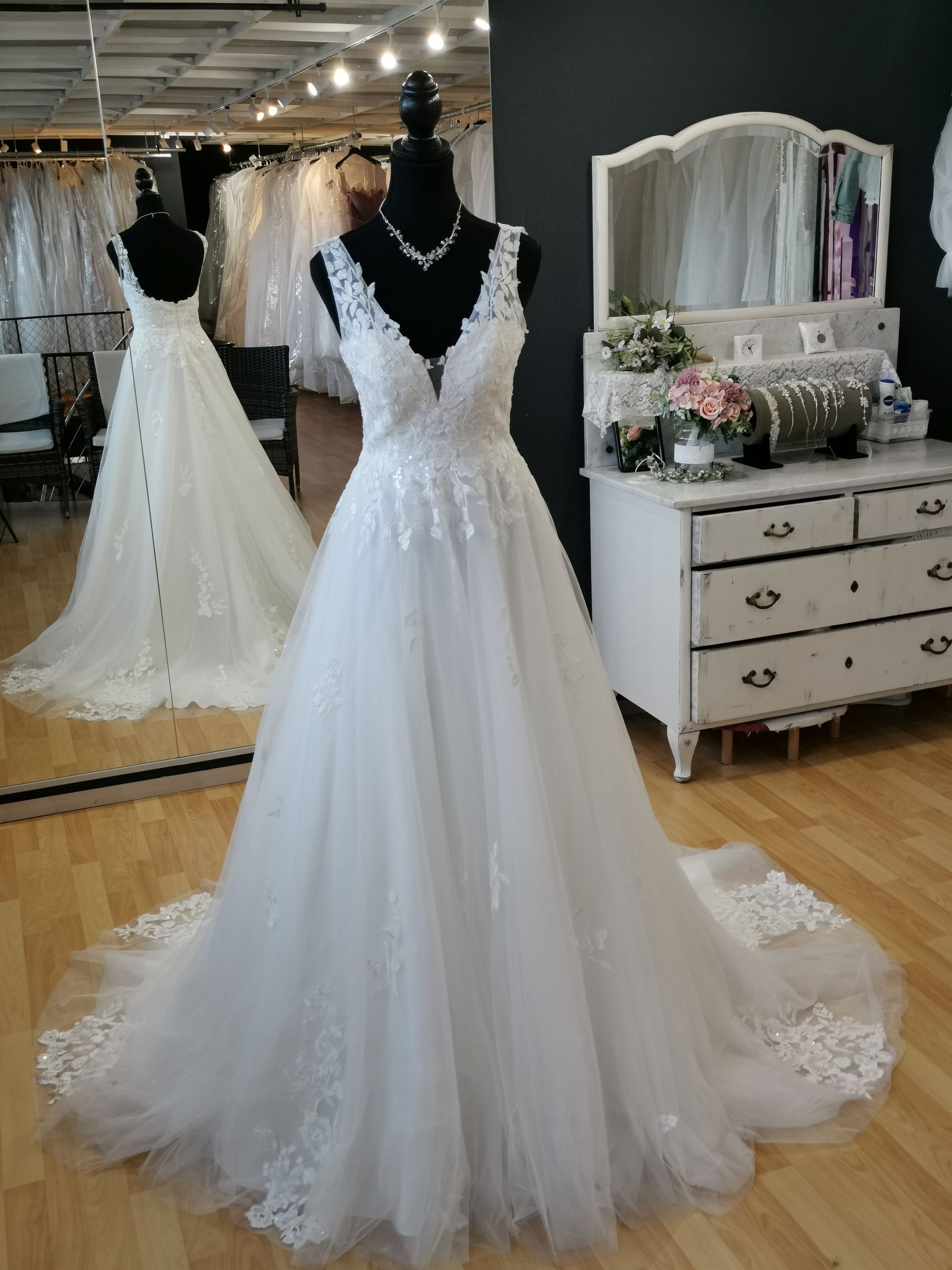 Weißes Spitzenhochzeitskleid mit Schleier und Tüllschleppe an einer Schaufensterpuppe in einem Brautmodengeschäft ausgestellt.