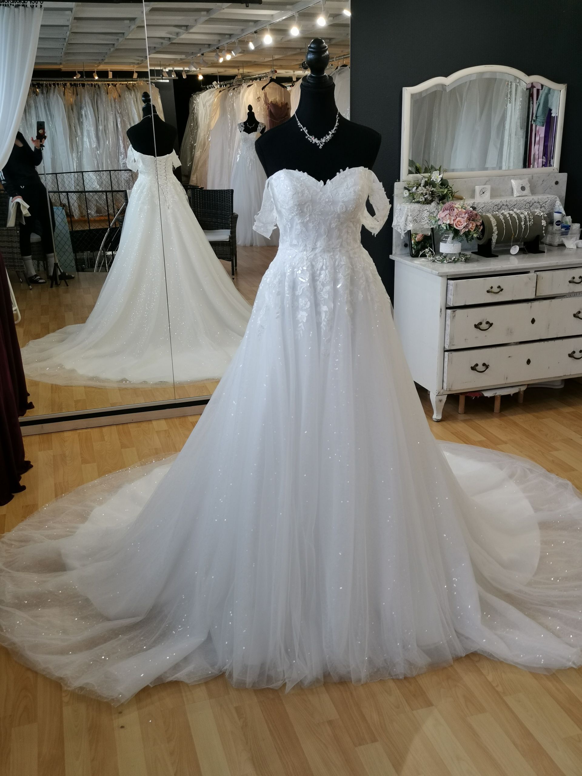Weißes, trägerloses Brautkleid an einer Schaufensterpuppe in einem Brautmodengeschäft, mit langer Schleppe und glitzerndem Tüllrock.