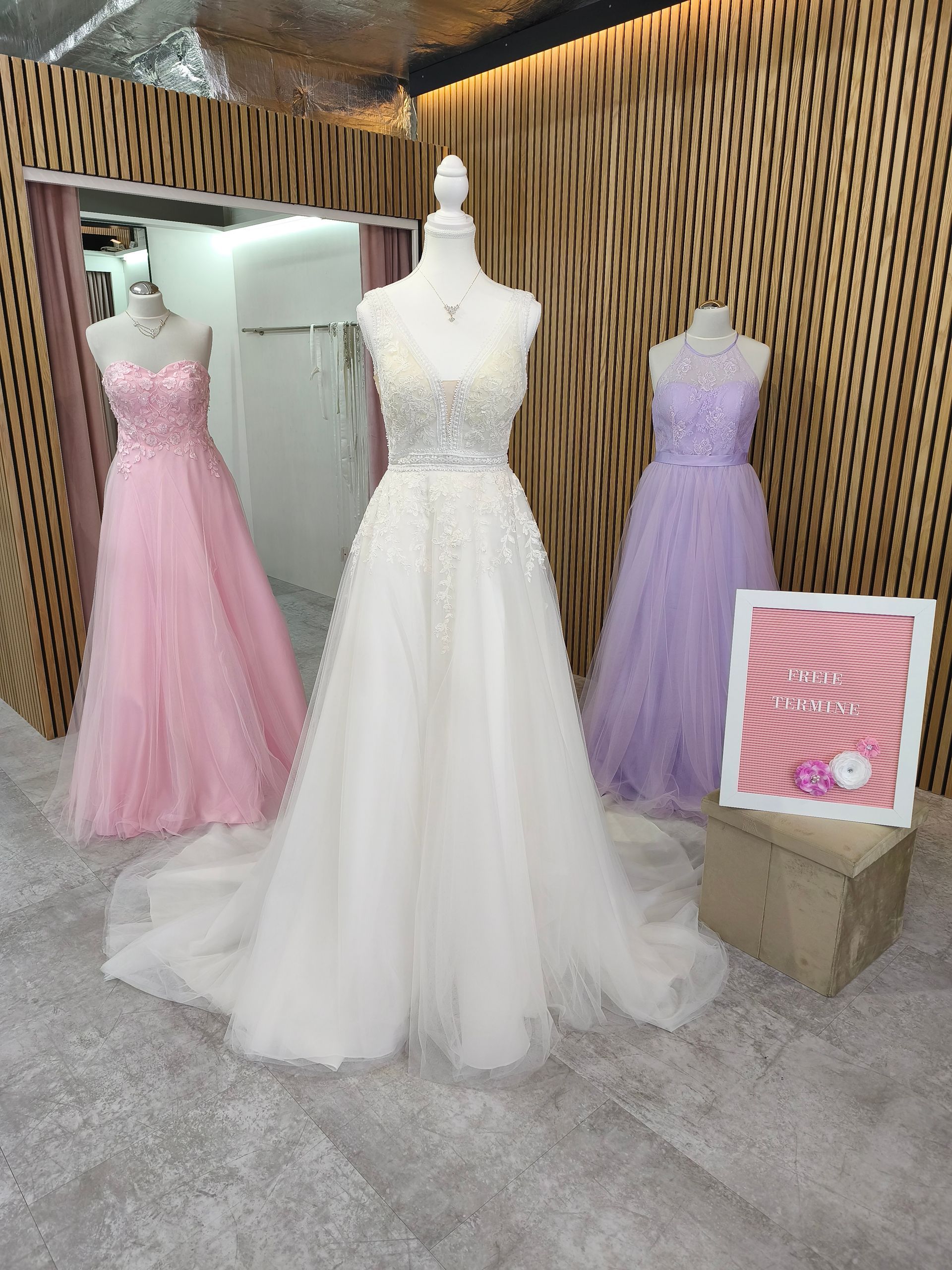 Schaufensterdekoration in einem Brautmodengeschäft mit drei Schaufensterpuppen in rosa, weißen und lavendelfarbenen Brautkleidern