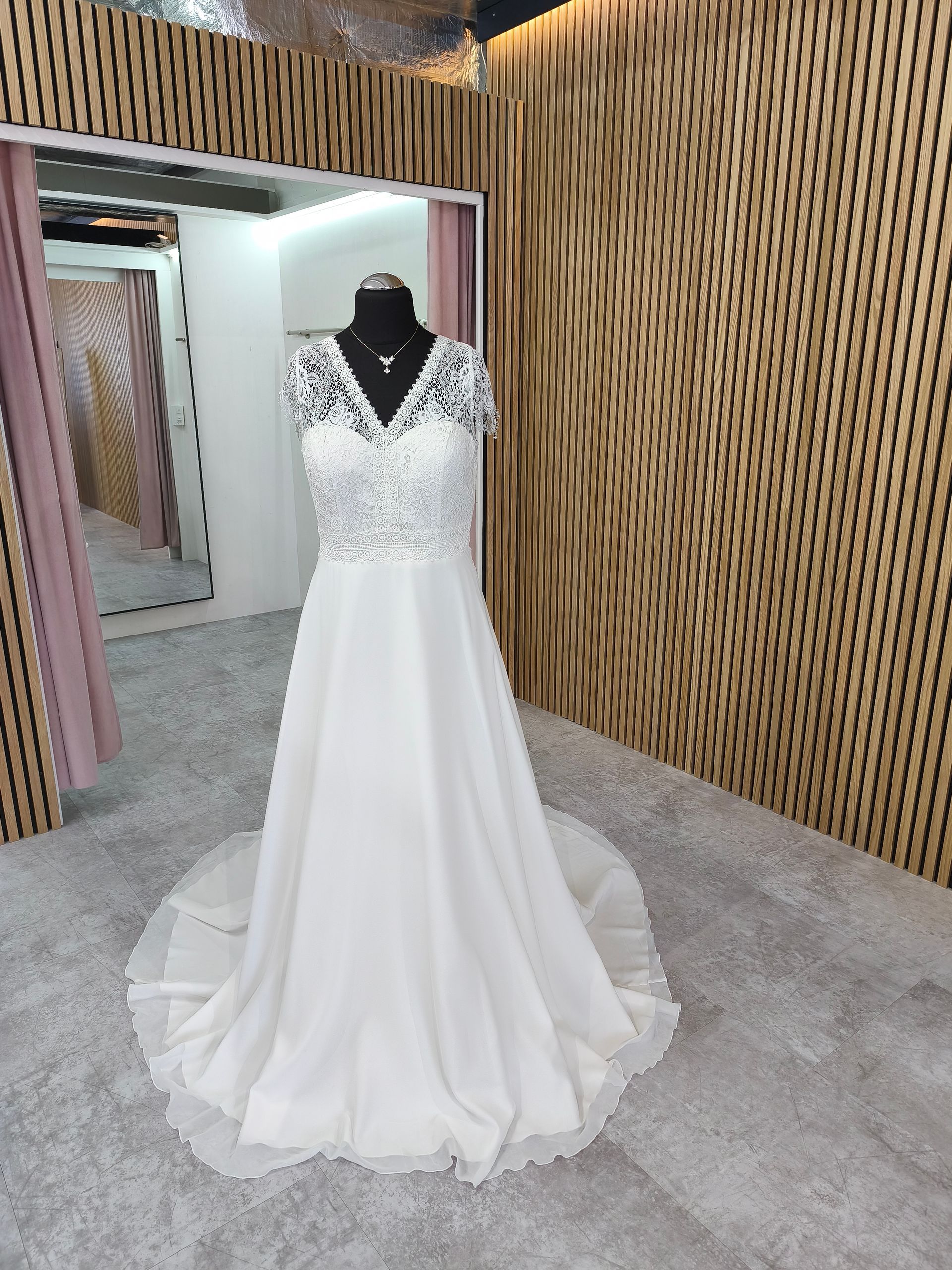 Weißes Brautkleid mit Spitzenoberteil an einer Schaufensterpuppe im Flur einer Brautboutique