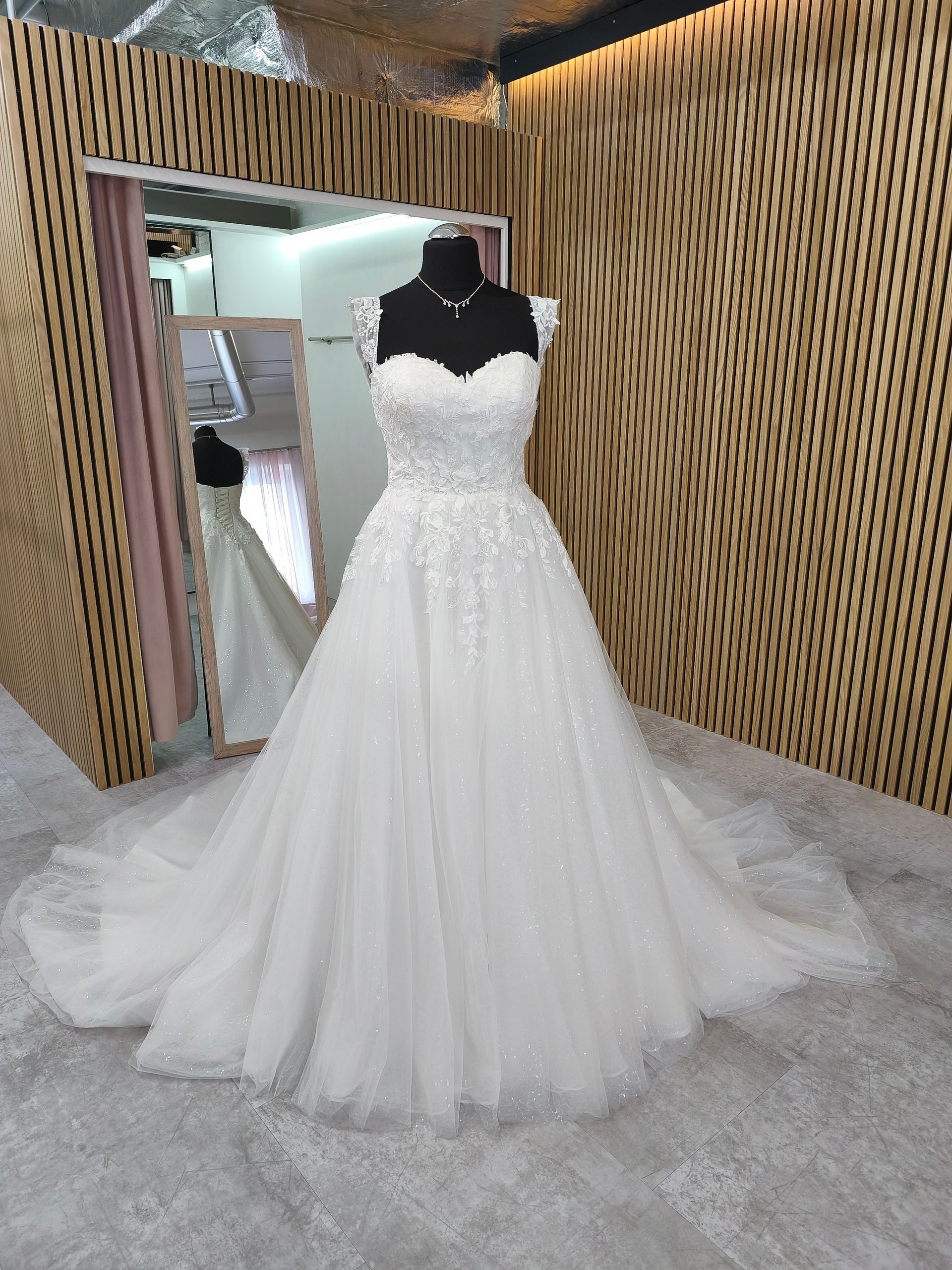 Weißes Brautkleid an einer Schaufensterpuppe in einem Brautmodengeschäft, mit langer Schleppe und Spitzendetails