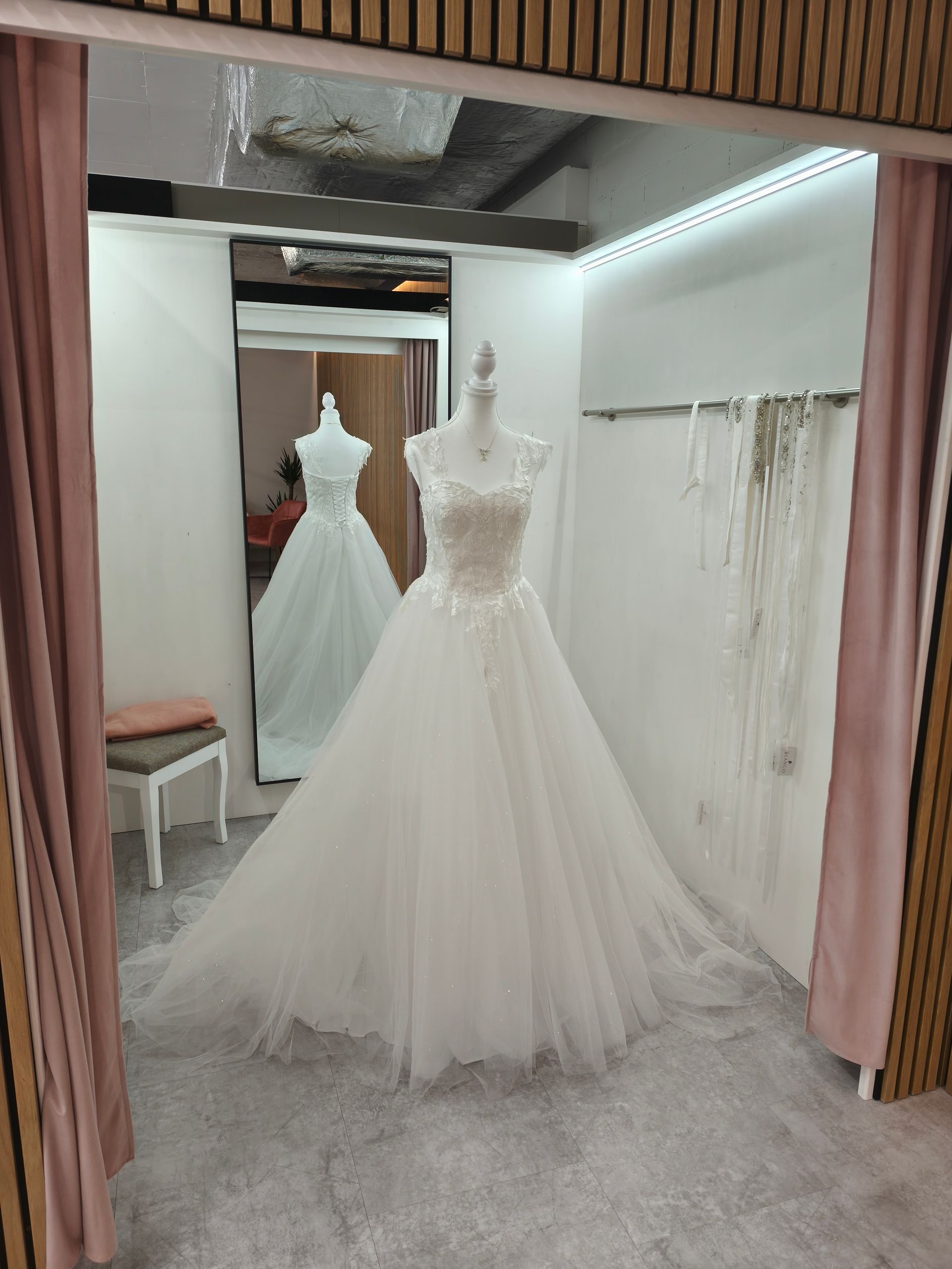 Brautboutique mit einem weißen Spitzenhochzeitskleid auf einer Schaufensterpuppe in einer verspiegelten Umkleidekabine