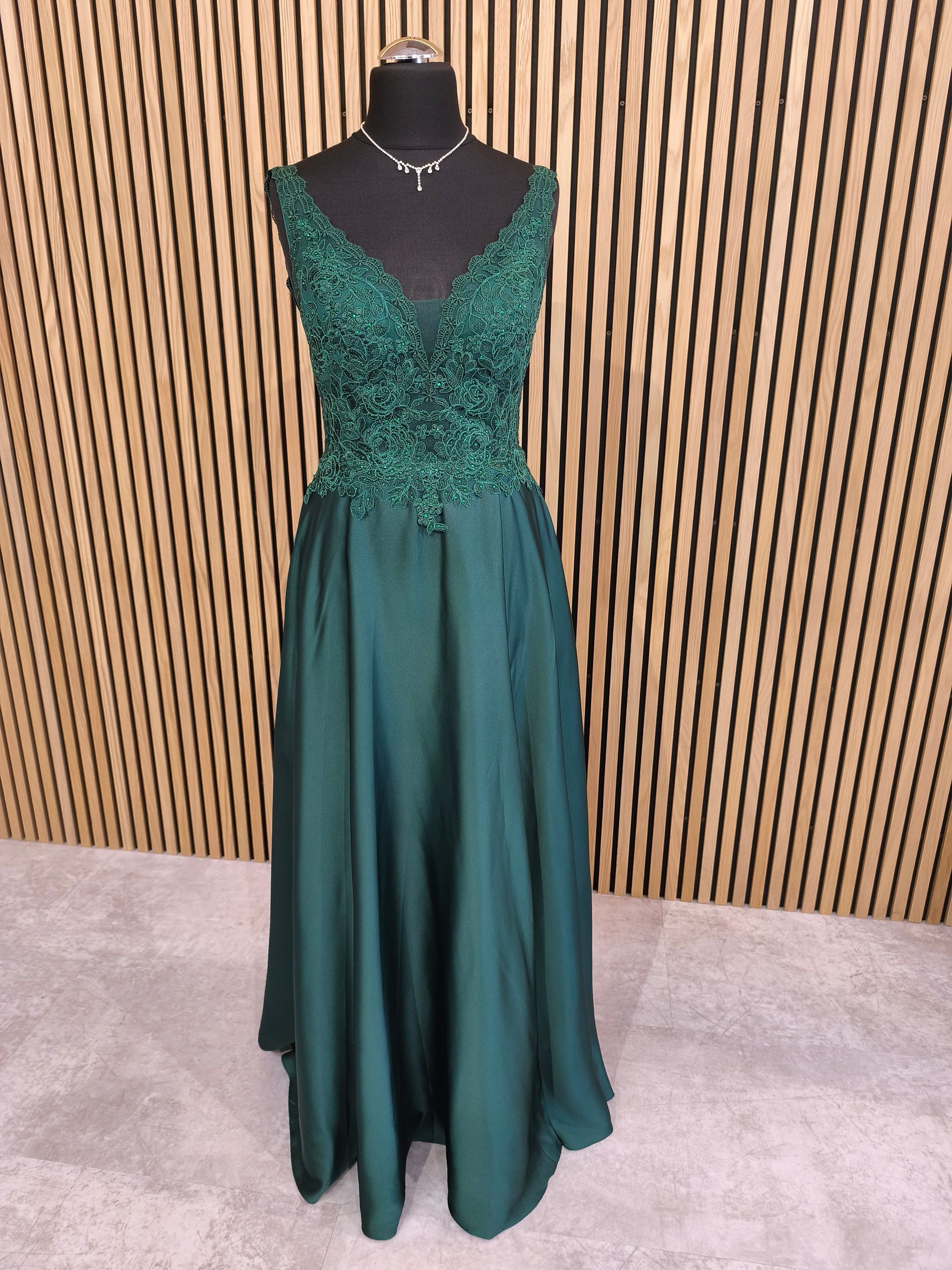 Smaragdgrünes, ärmelloses Abendkleid auf einer schwarzen Schaufensterpuppe vor einem Hintergrund aus Holzlatten