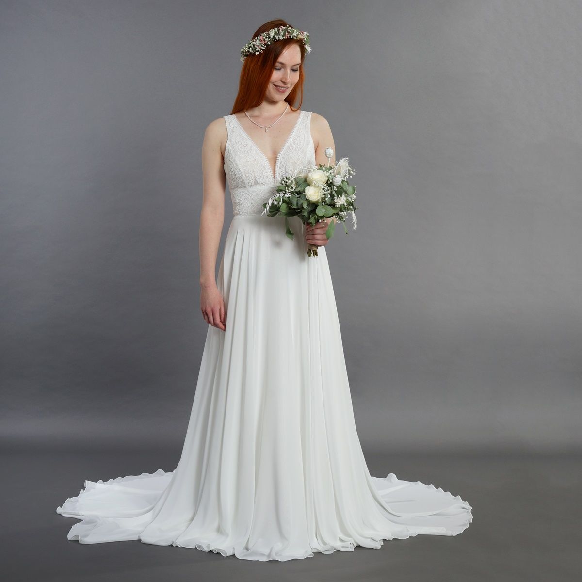 Frau in einem weißen Brautkleid mit einem Brautstrauß vor grauem Studiohintergrund