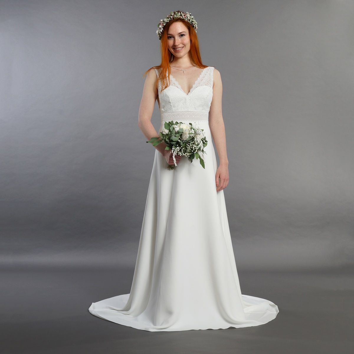 Frau in einem weißen Brautkleid hält einen Brautstrauß vor grauem Studiohintergrund