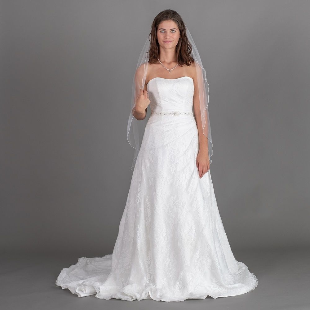 Braut in weißem Hochzeitskleid und Schleier vor grauem Studiohintergrund.