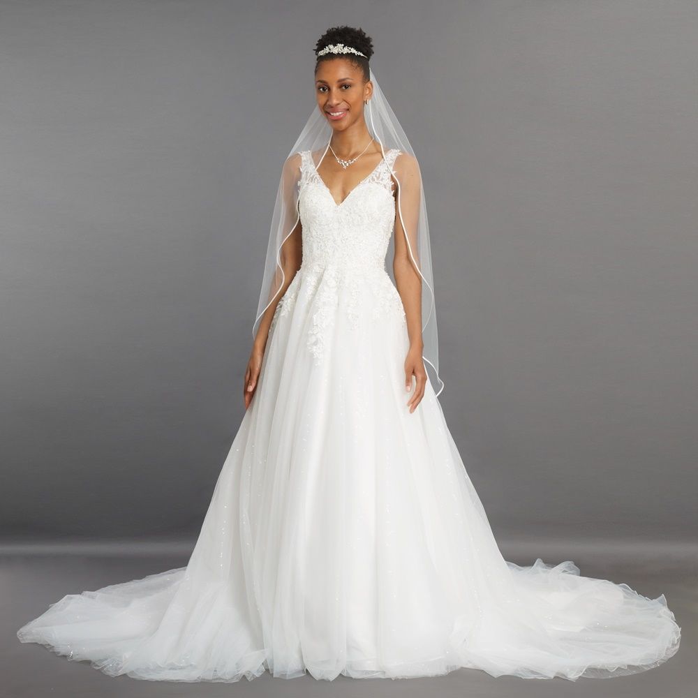Braut in einem trägerlosen weißen Hochzeitskleid mit langem Schleier und Schleppe, vor grauem Hintergrund