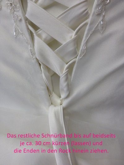 Weiße Korsettschnürung wird am Rücken eines weißen Kleides entlanggeführt, unten befindet sich ein deutscher Anweisungstext.
