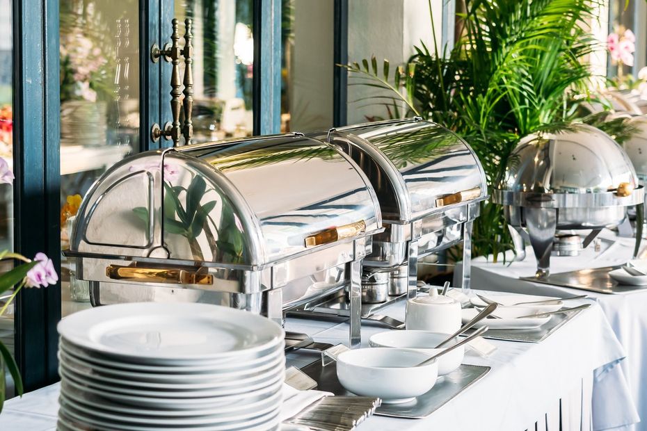 A buffet table with plates , bowls , and silverware on it.