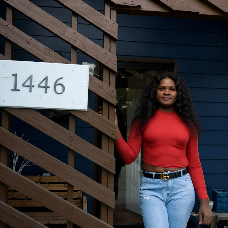 Woman standing in a doorway beside a house number sign reading 1446