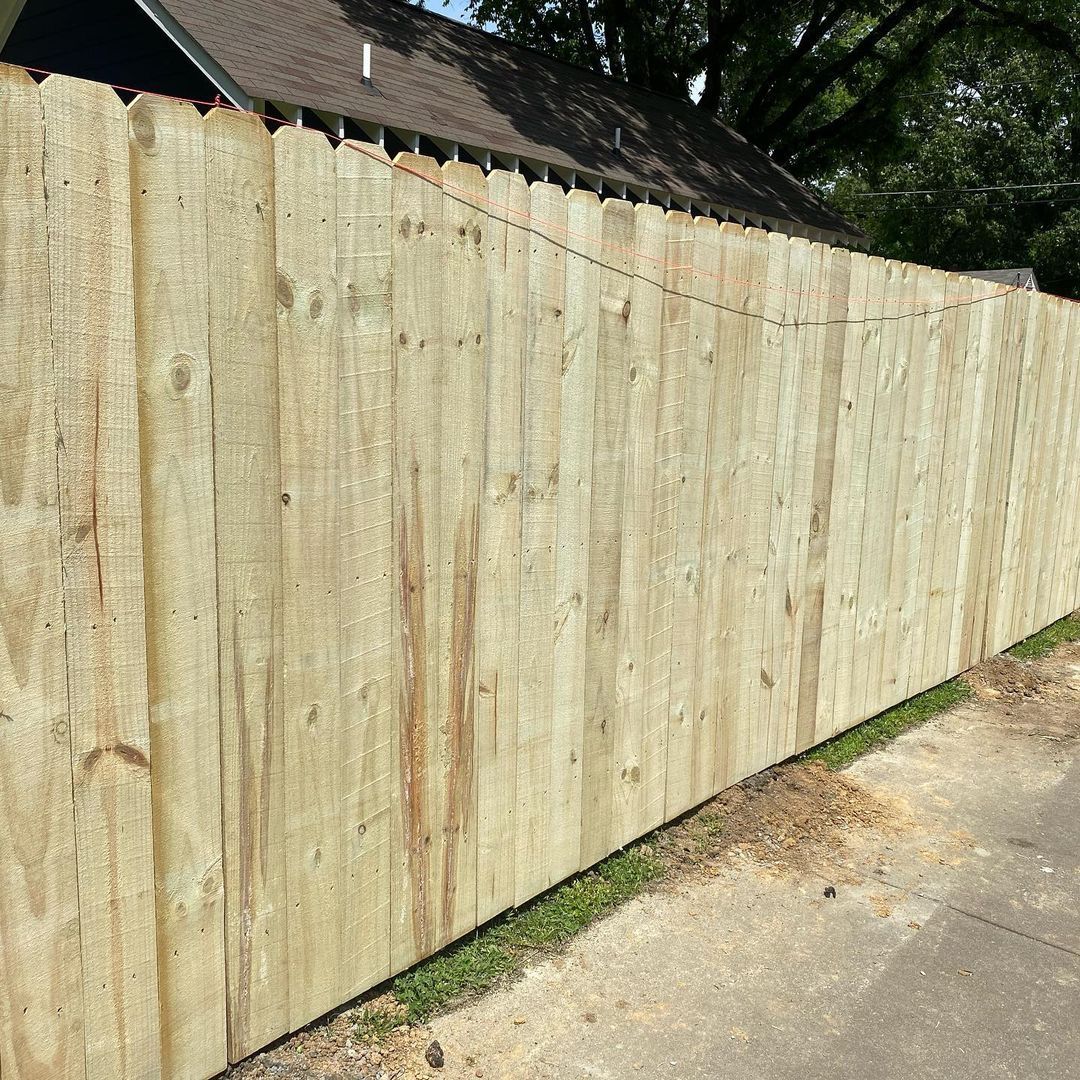 Sunlit wooden privacy fence beside a concrete sidewalk and grass strip
