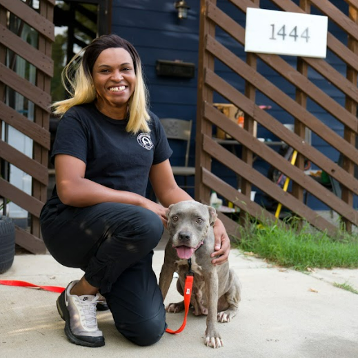 Woman kneels beside a gray dog on a red leash in front of a house numbered 1444.